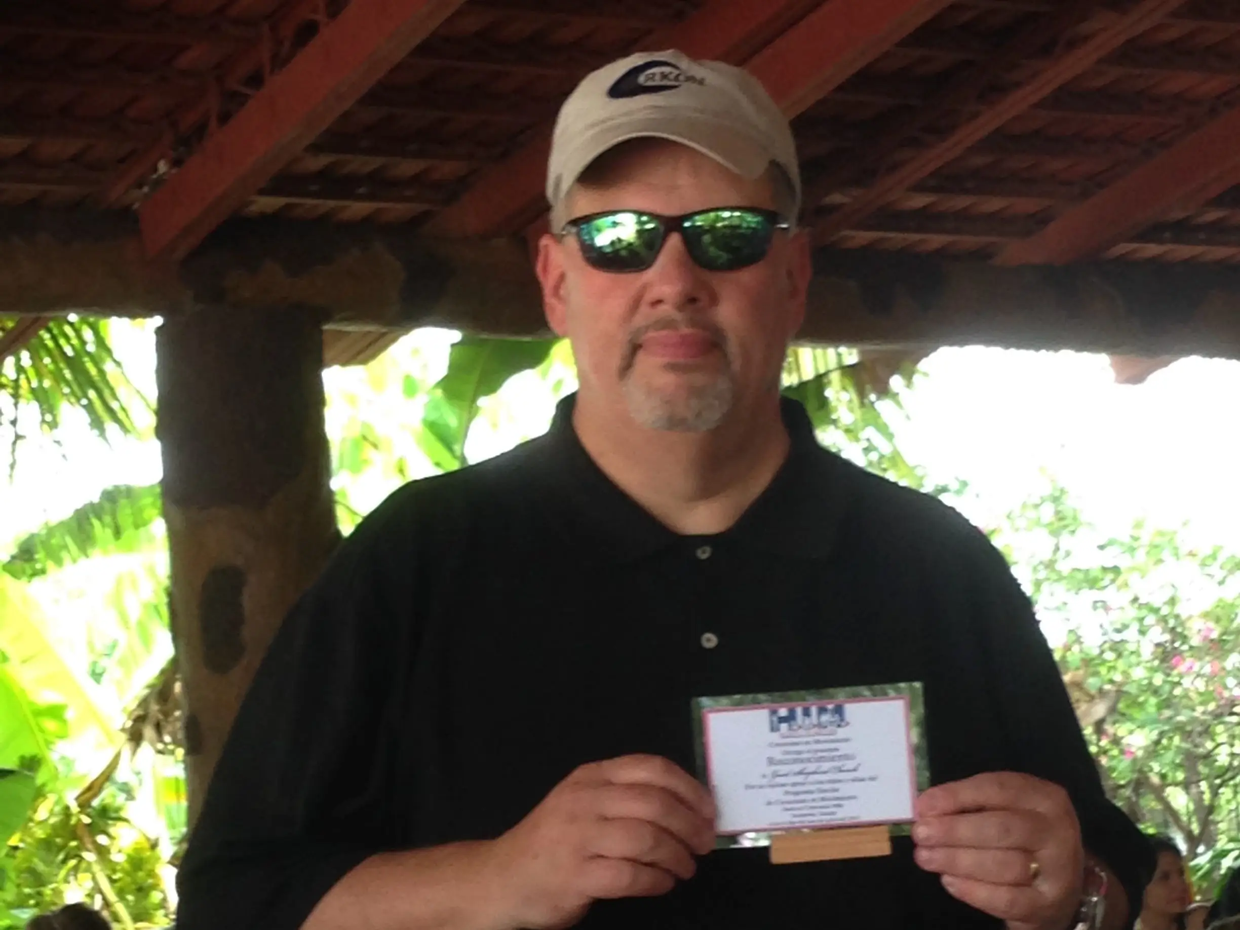 An overweight man in a black shirt and beige baseball cap.