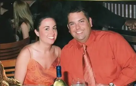 Sitting together at a restaurant table, a smiling couple in orange outfits pose.