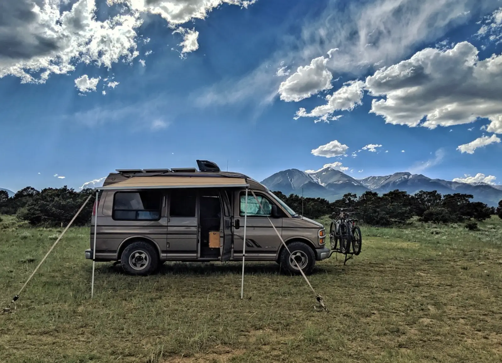A van parked in the grass in Colorado, with mountains in the background and clouds in the sky.