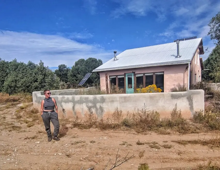 The writer standing in front of a pink house in rural New Mexico.