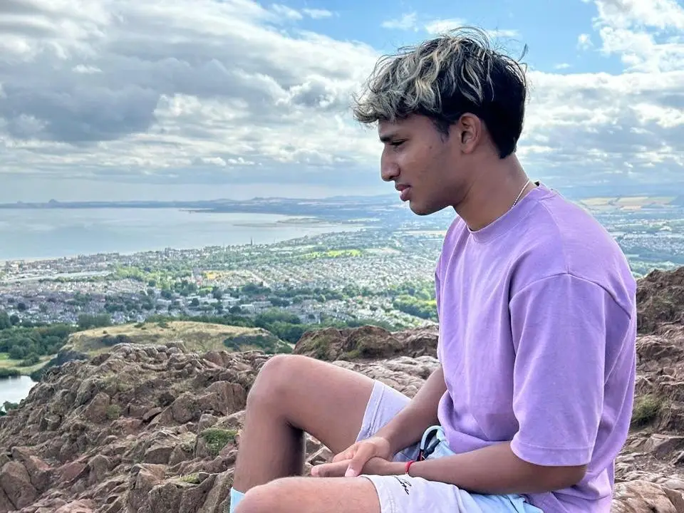 A man sitting on rocks, looking out to the sea in the distance.