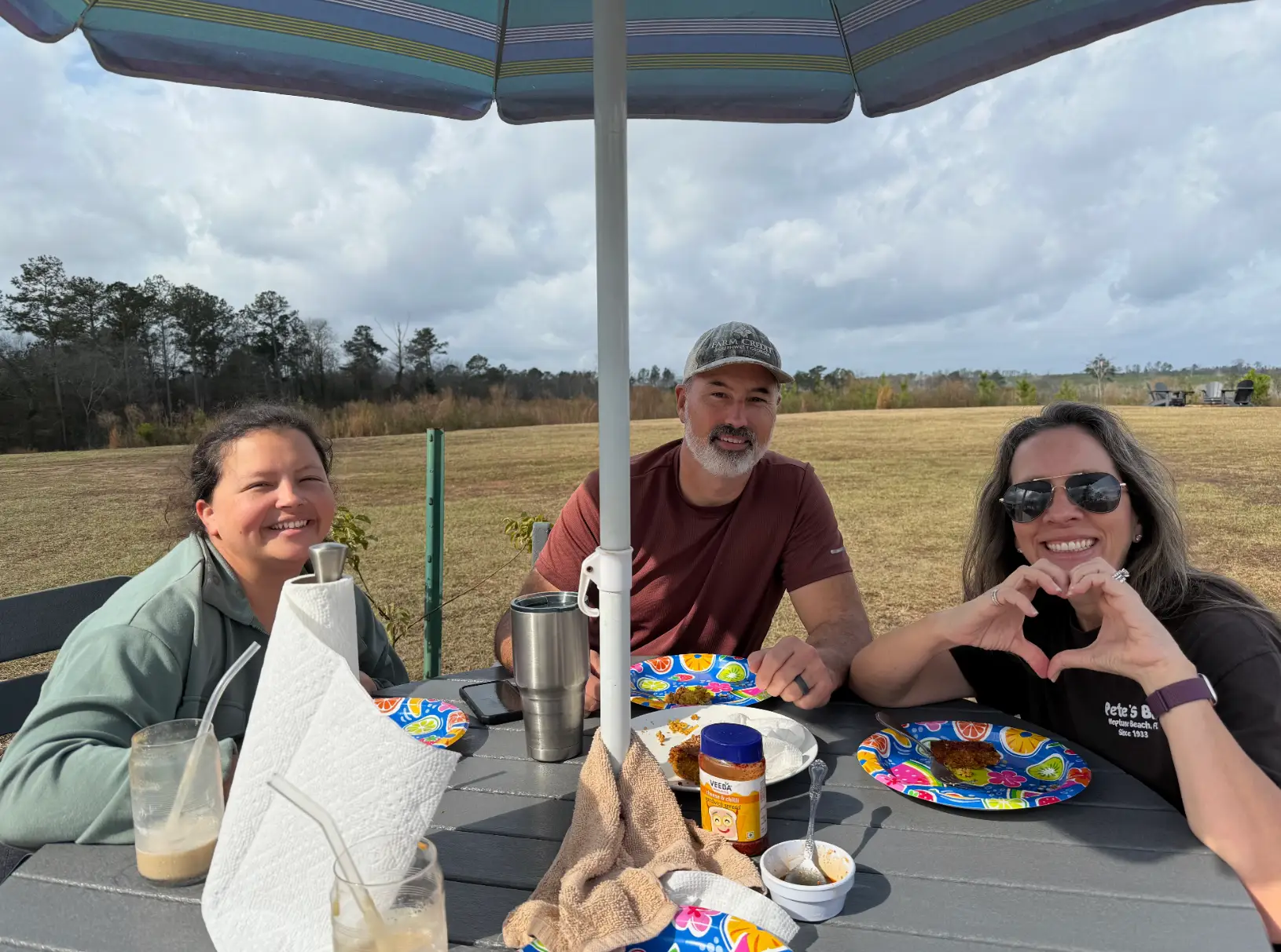 Three people sitting around a table, eating food, with a field in the background.