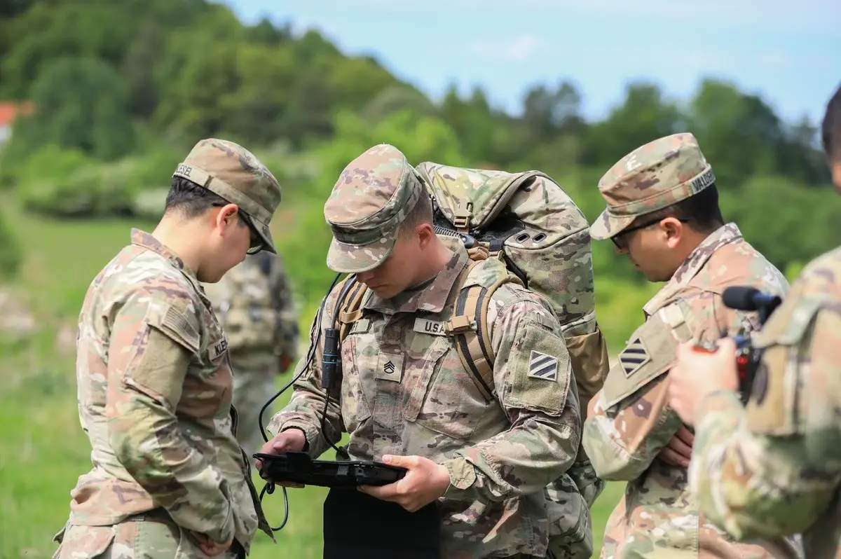 A group of soldiers stands around a tablet in the forest.