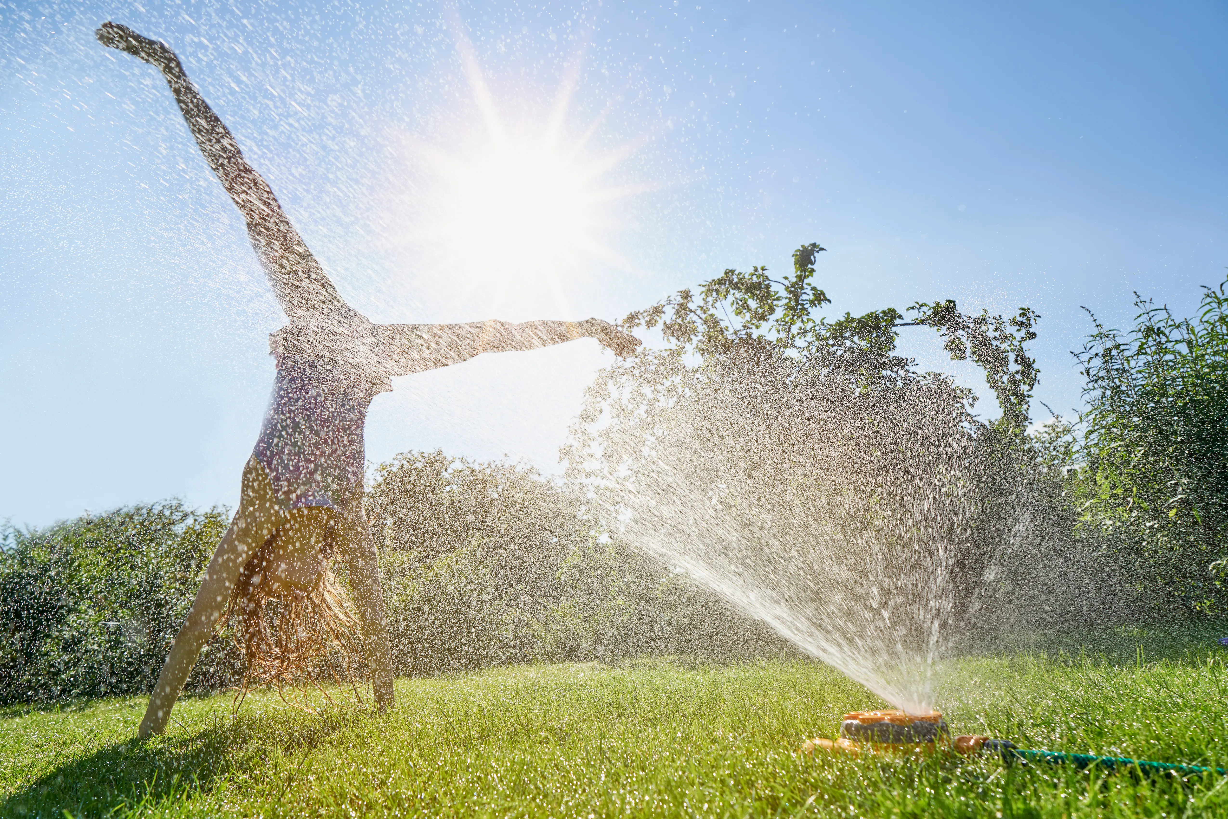 A teen does a cartwheel in a sprinkler.