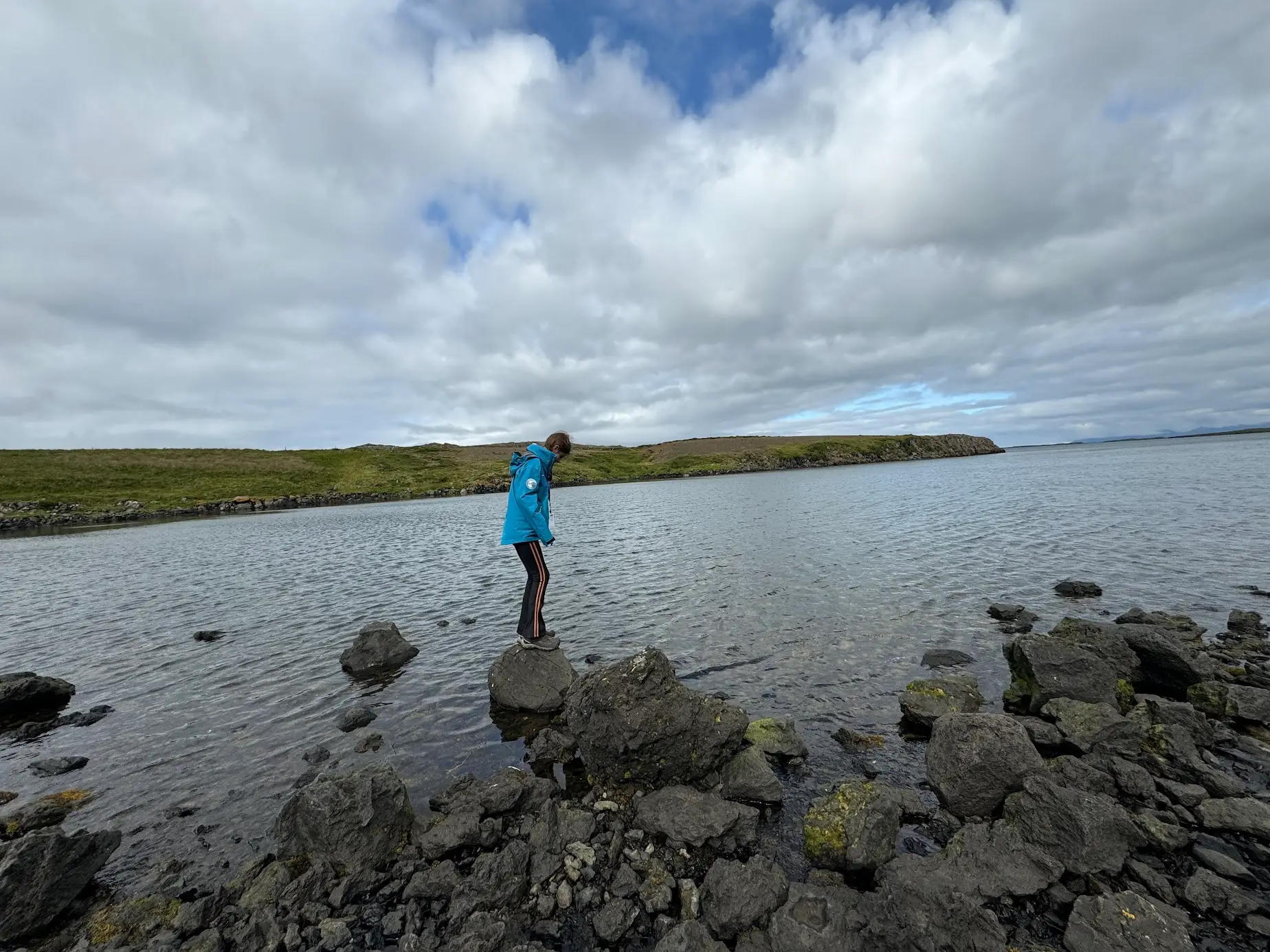 A young girl plays on rocks by a lake.
