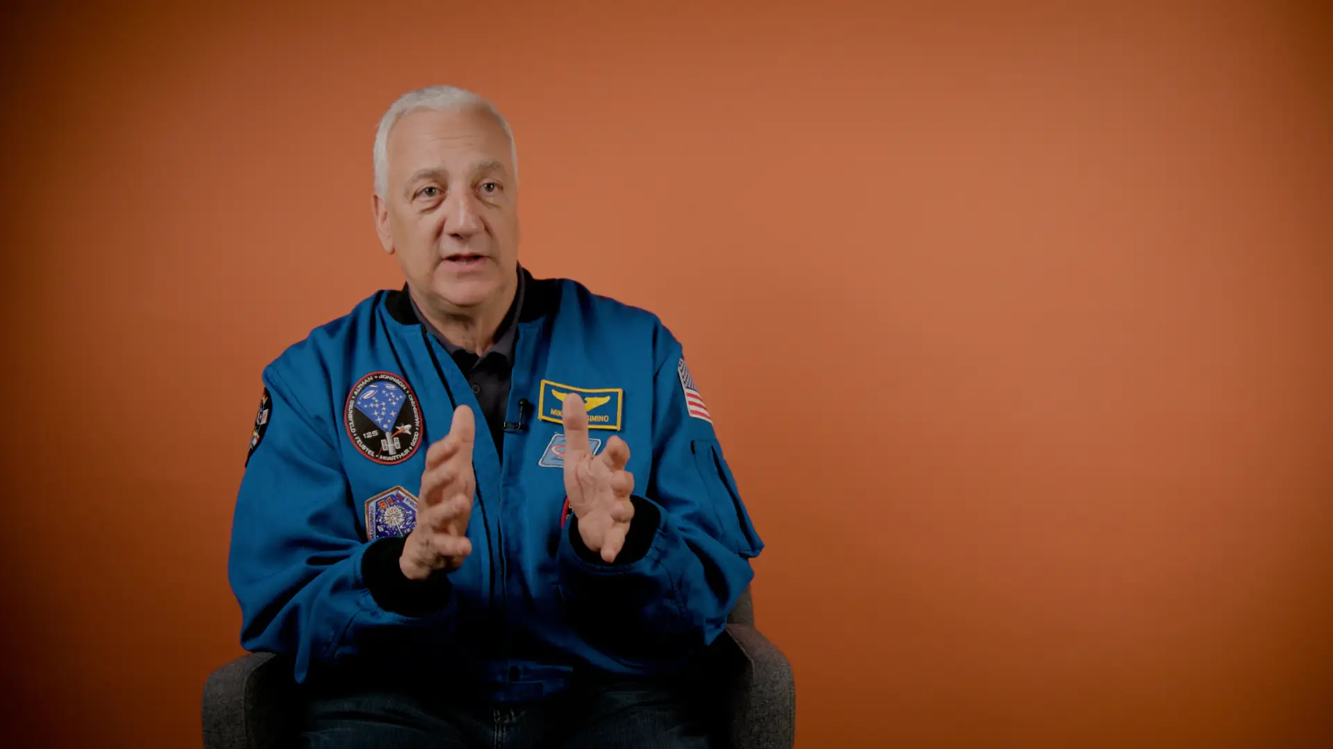 Mike Massimino in a blue NASA jacket with patches on it.