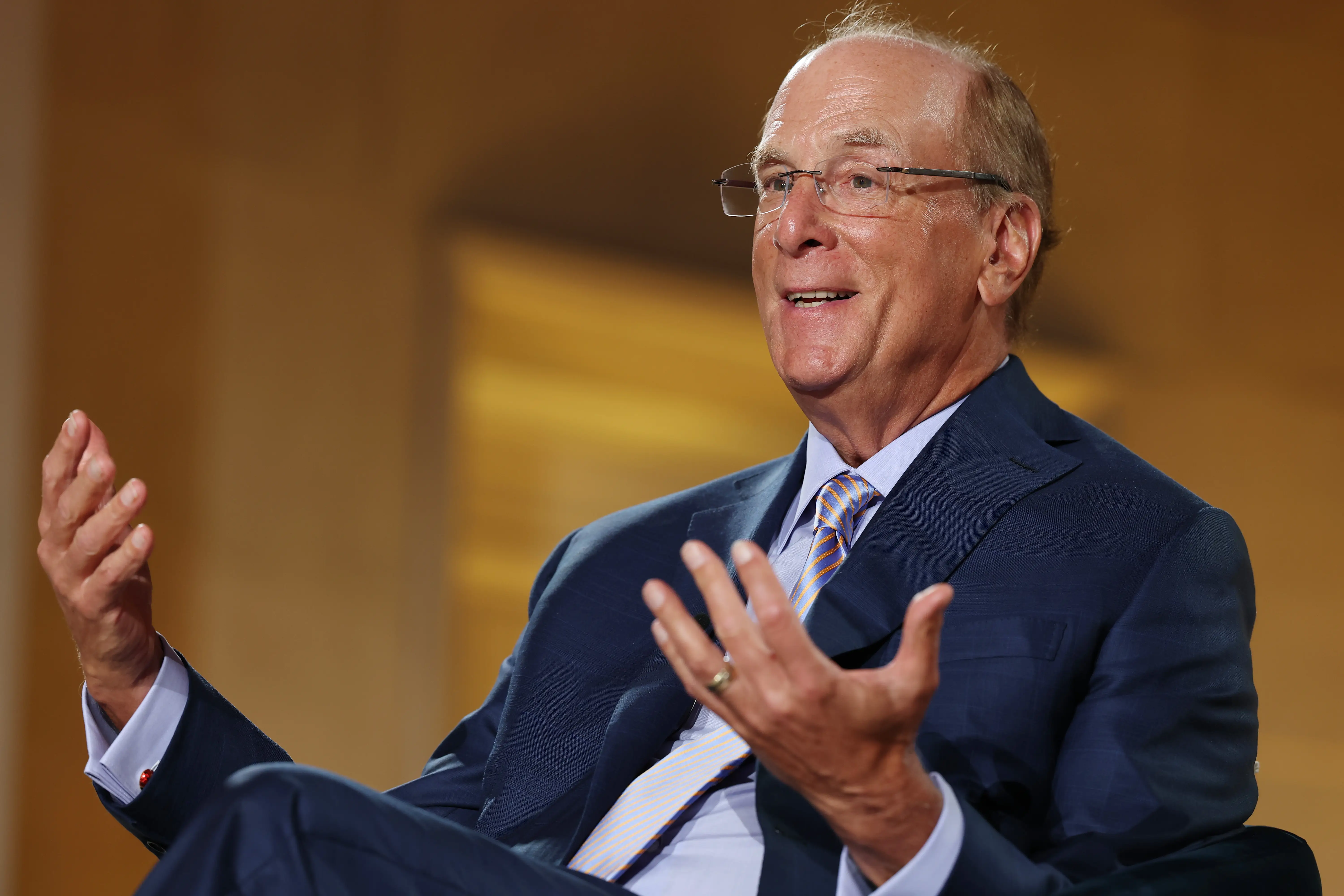 Larry Fink sits onstage in a dark blue suit
