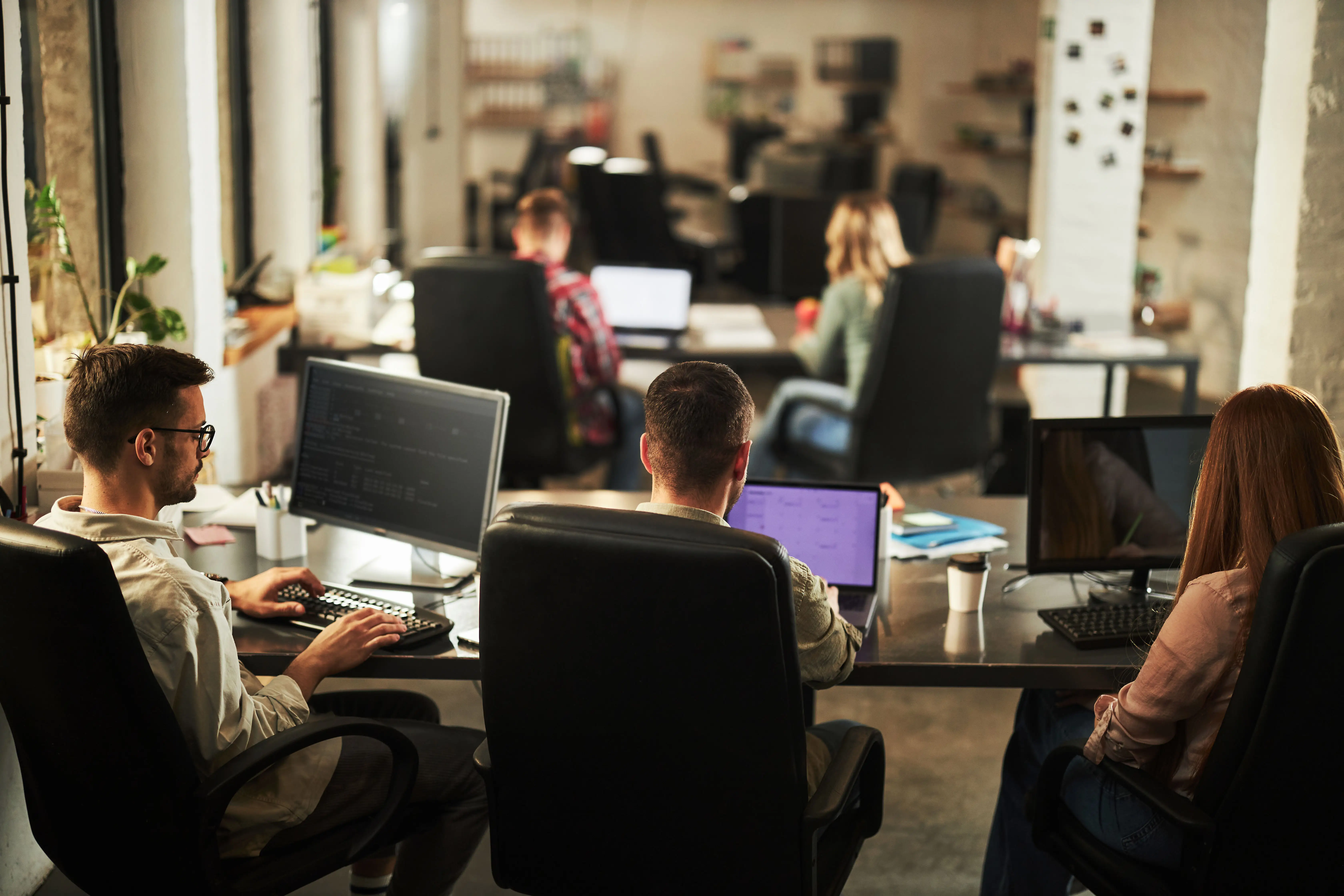 Back view of team of graphic designers working on computers in the office.