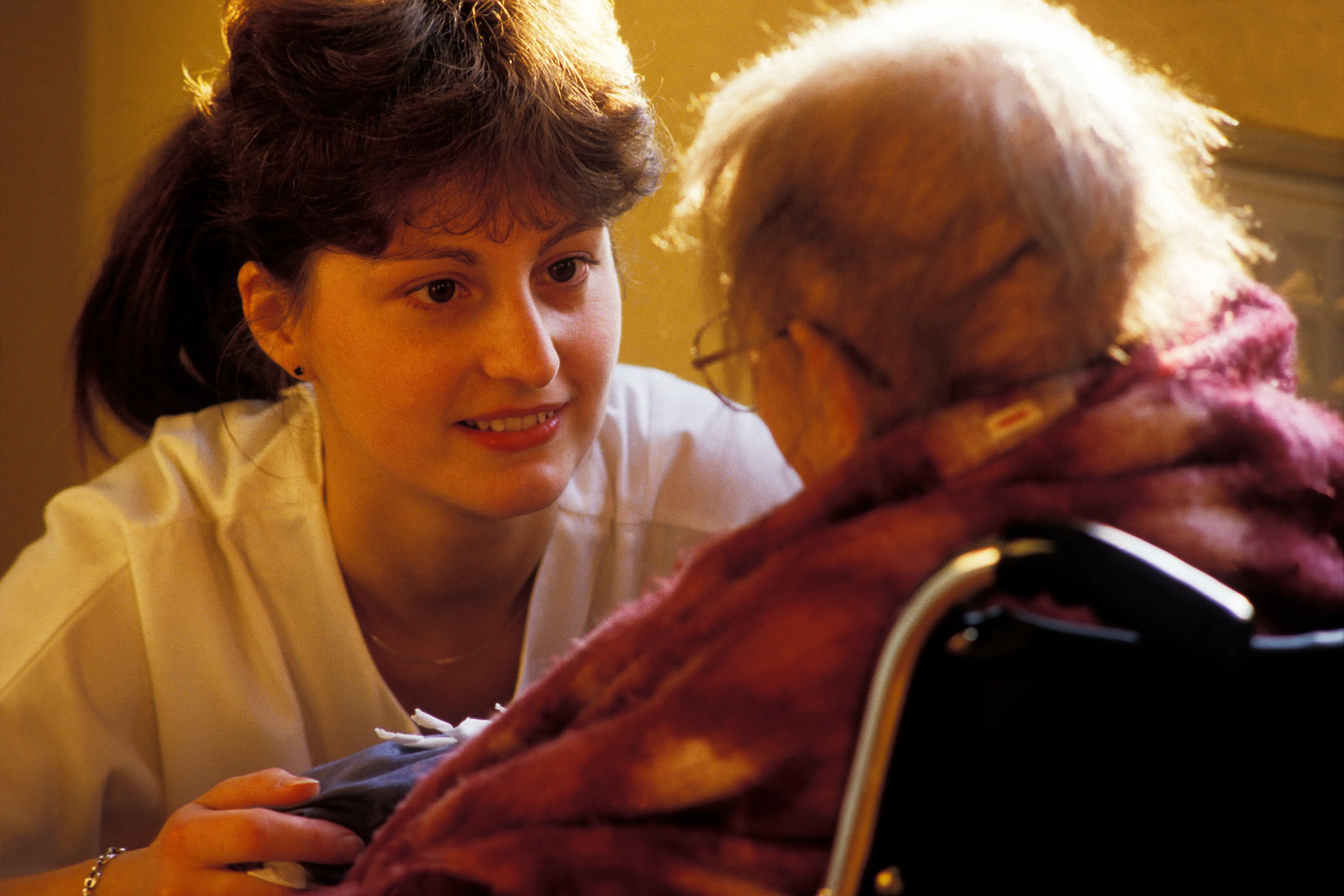 A younger woman looks at an older woman in a nursing home.