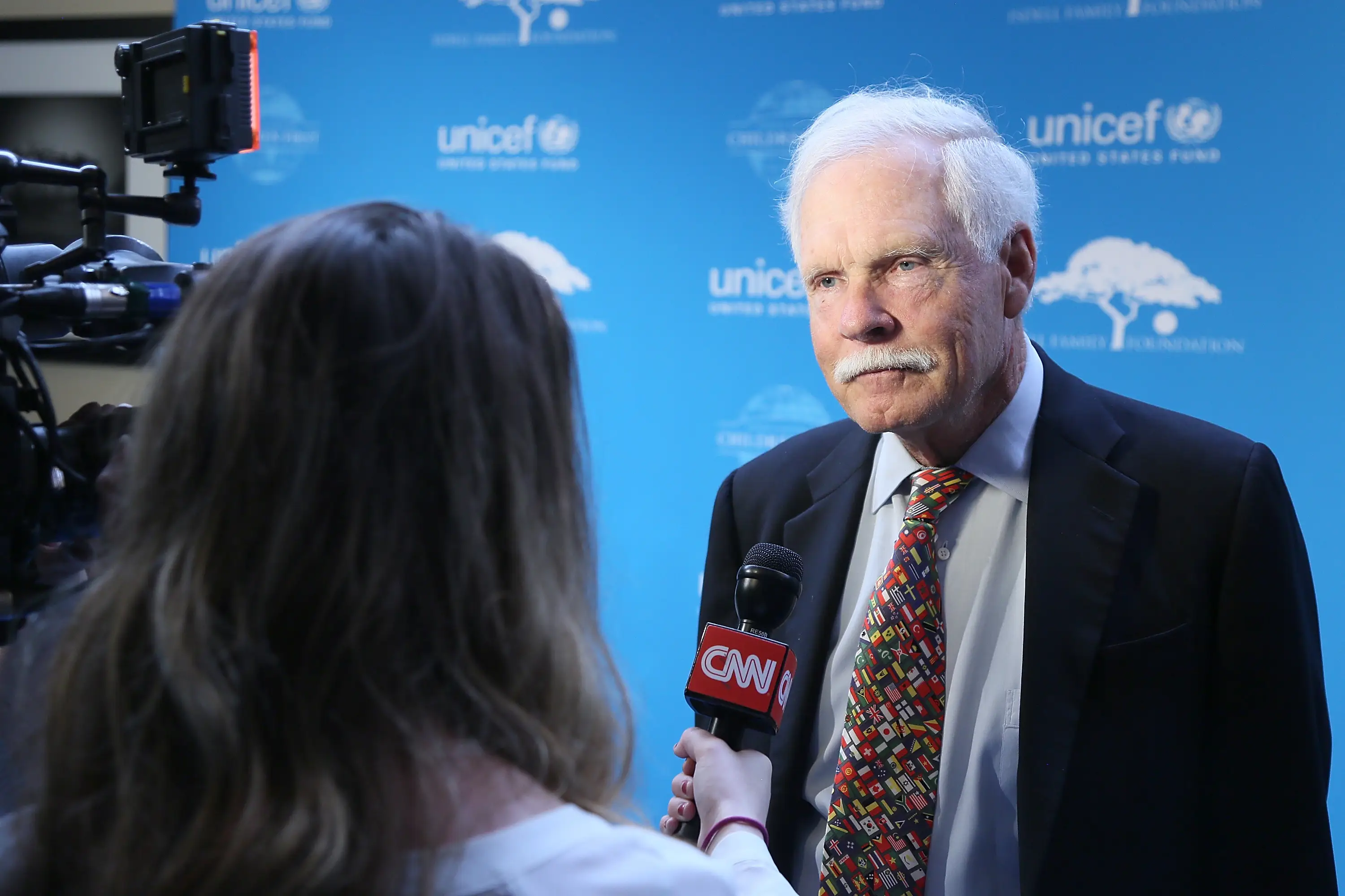 Ted Turner, the media mogul who founded CNN, talks to a reporter while standing before a UNICEF step-and-repeat.