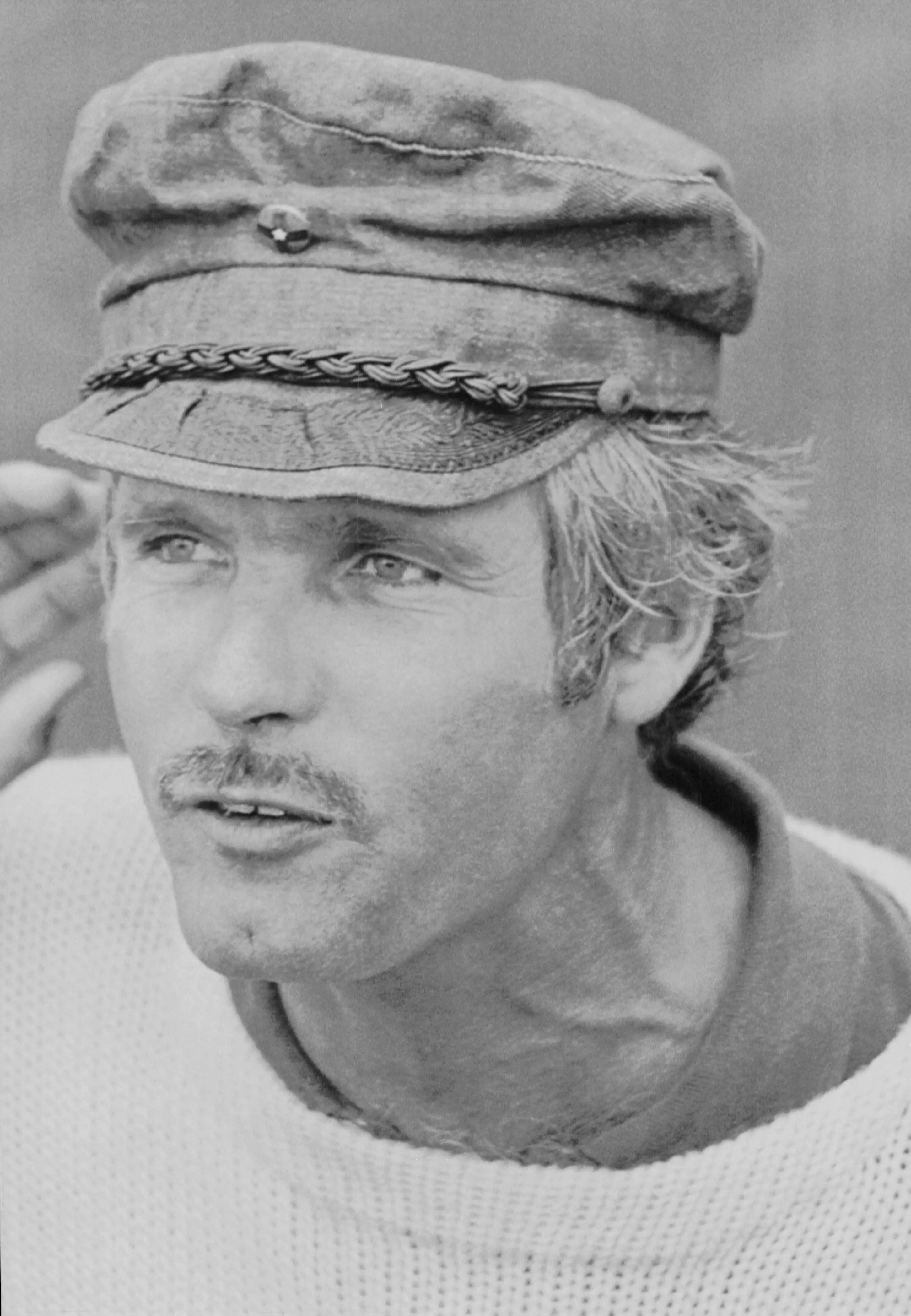 Ted Turner, wearing a sailing cap, cups his ear as he listens to onlookers at a yachtsman competition.