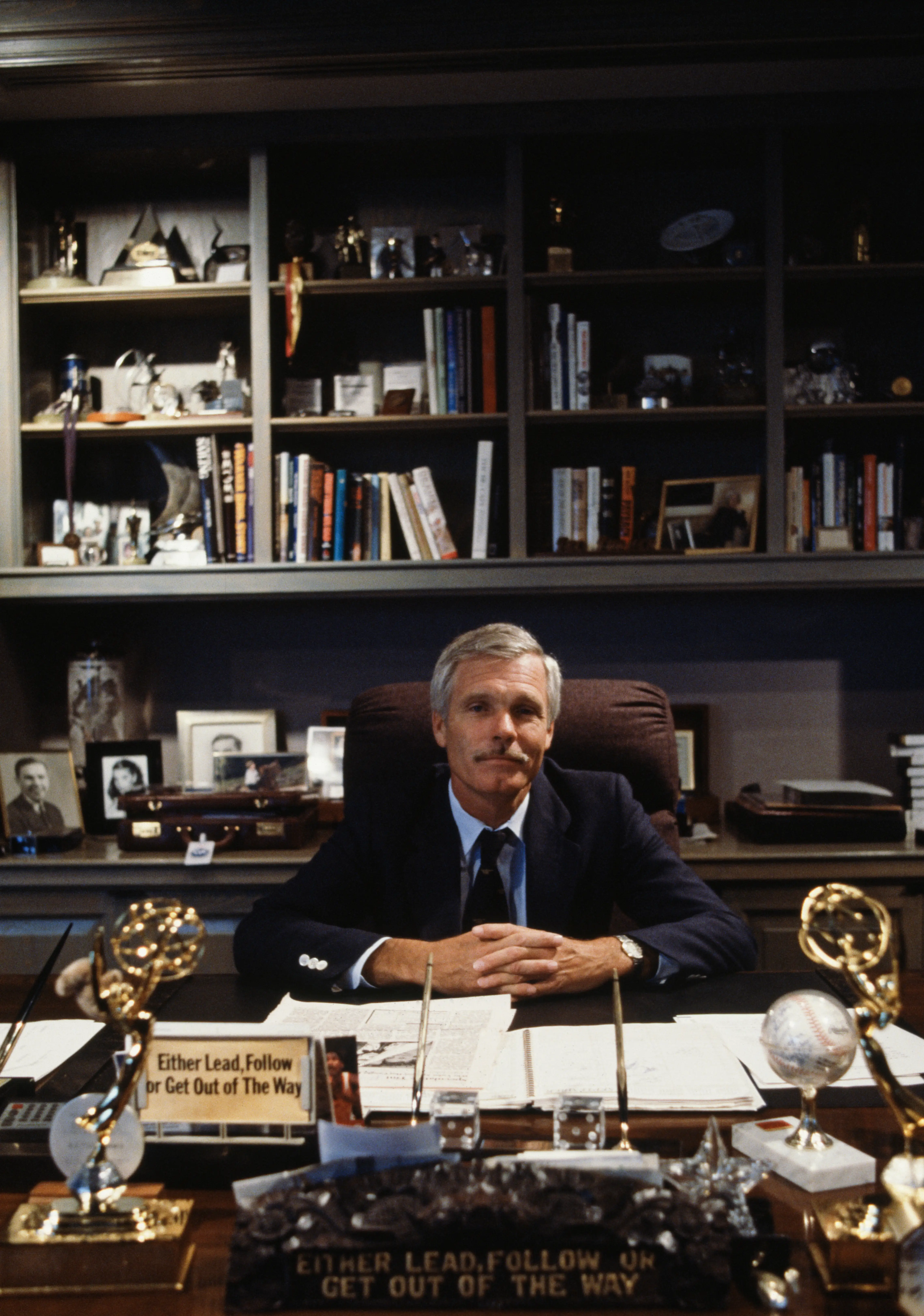 Ted Turner is sitting with his fingers interlaced inside his home office.