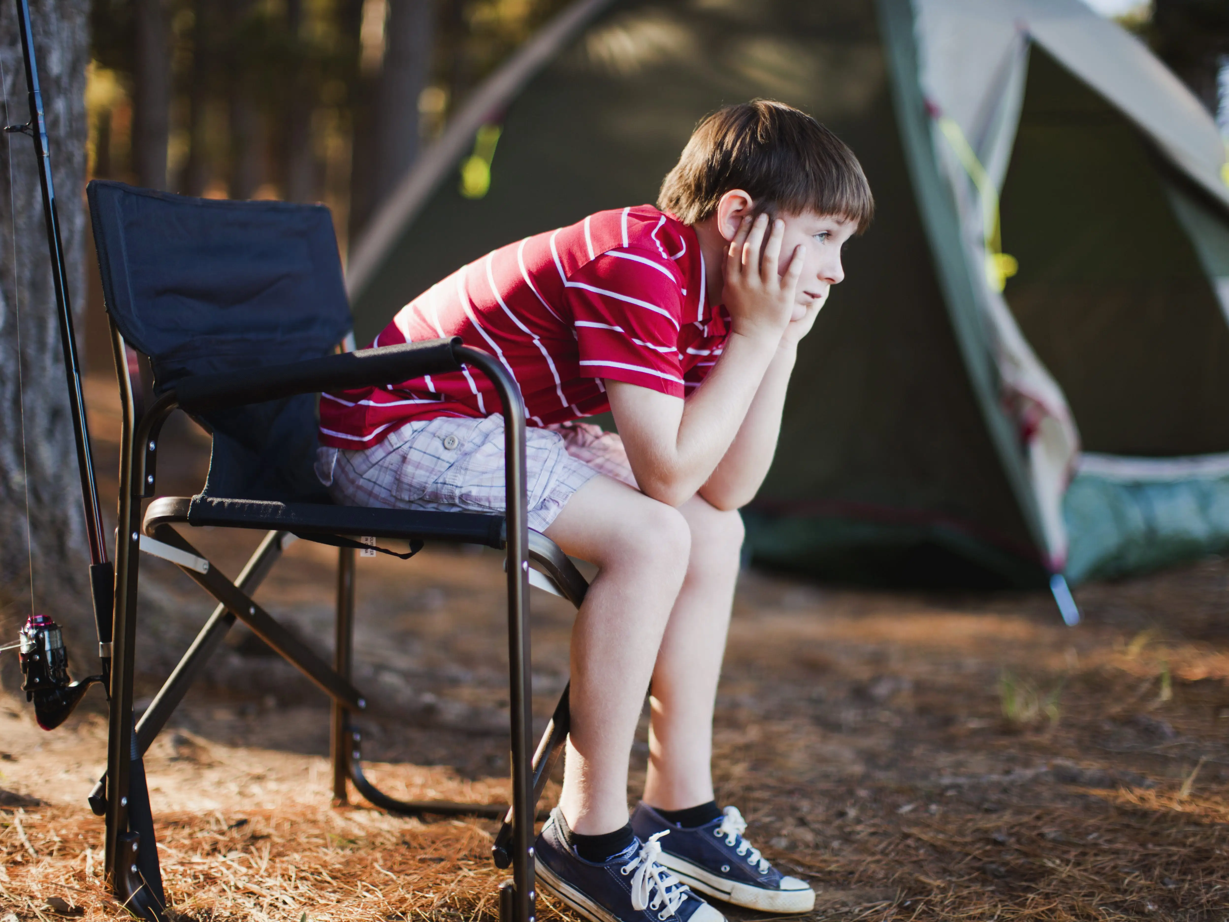 an upset kid sitting on a camping chair in summer camp