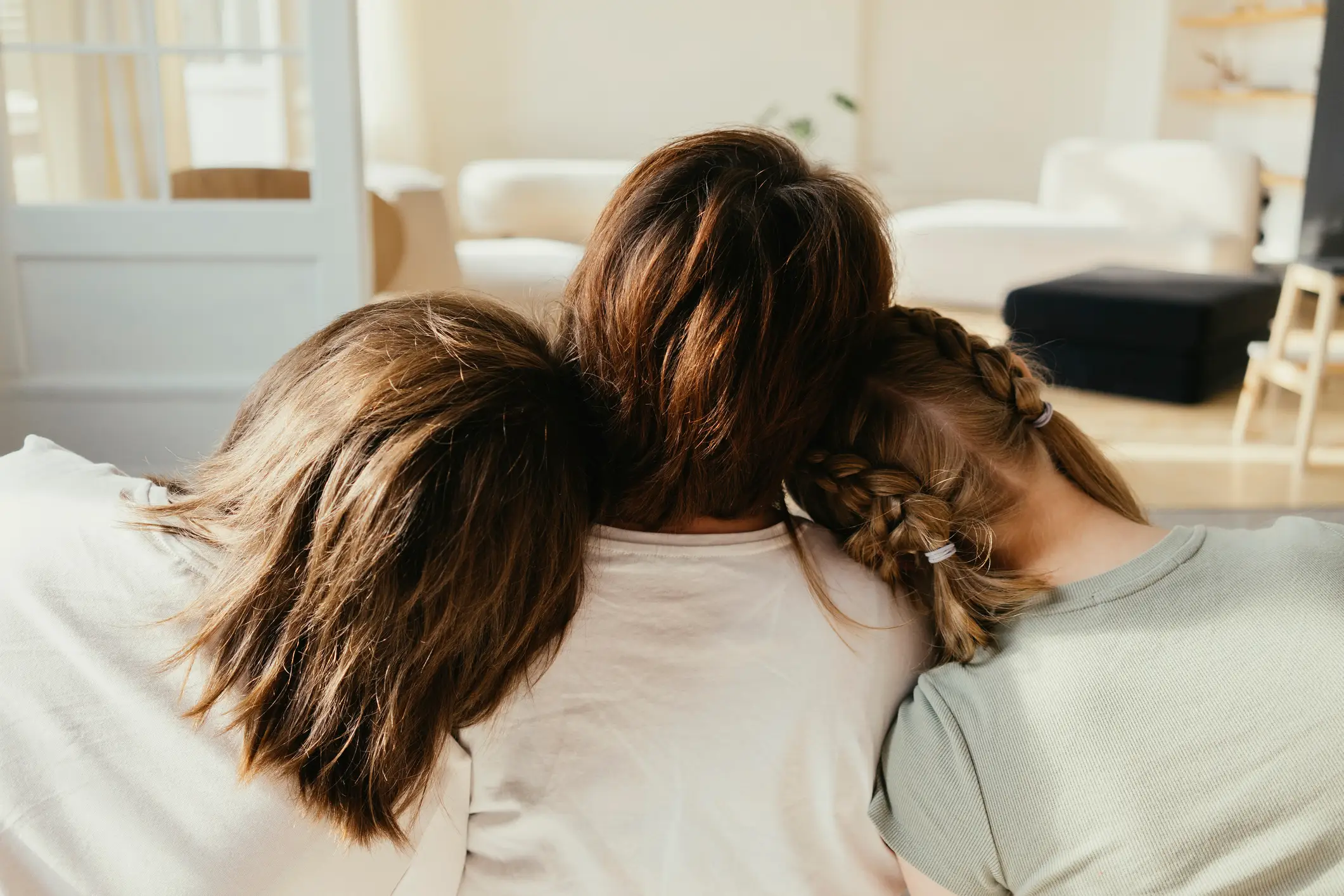 The backs of three women's heads as they sit on a couch and stare ahead.