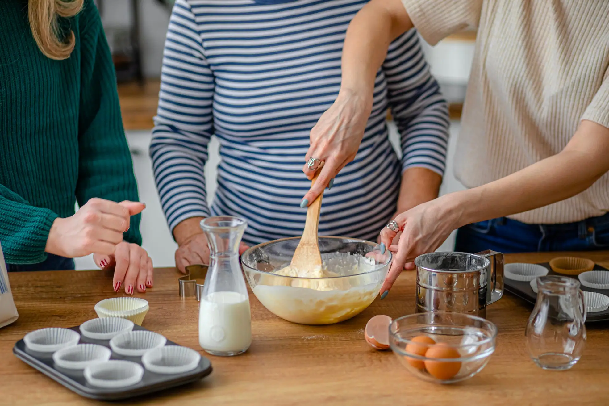 Three women standing around a table, baking something together.