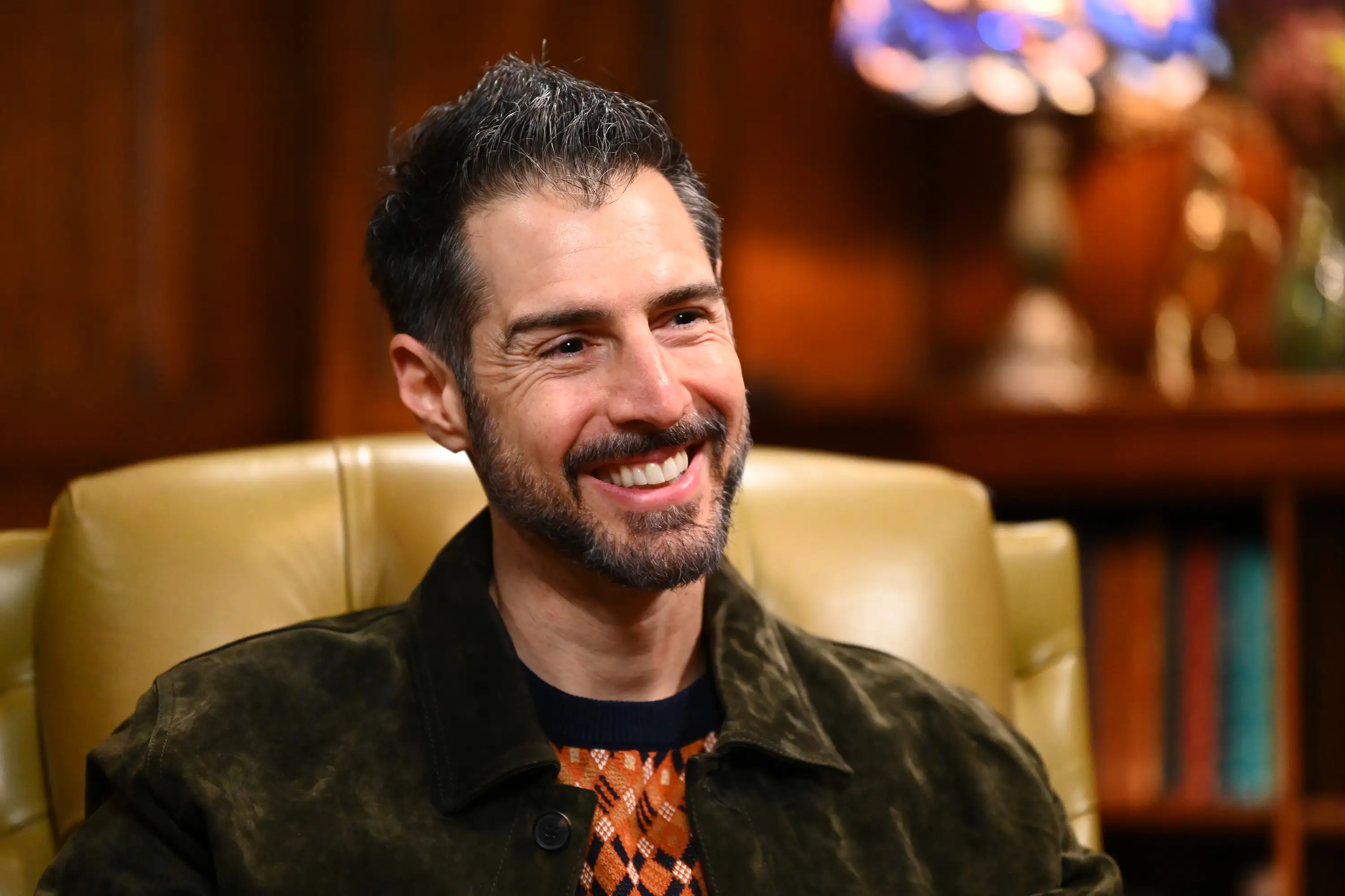 Rob Cesternino smiles sitting in a chair on the set of 