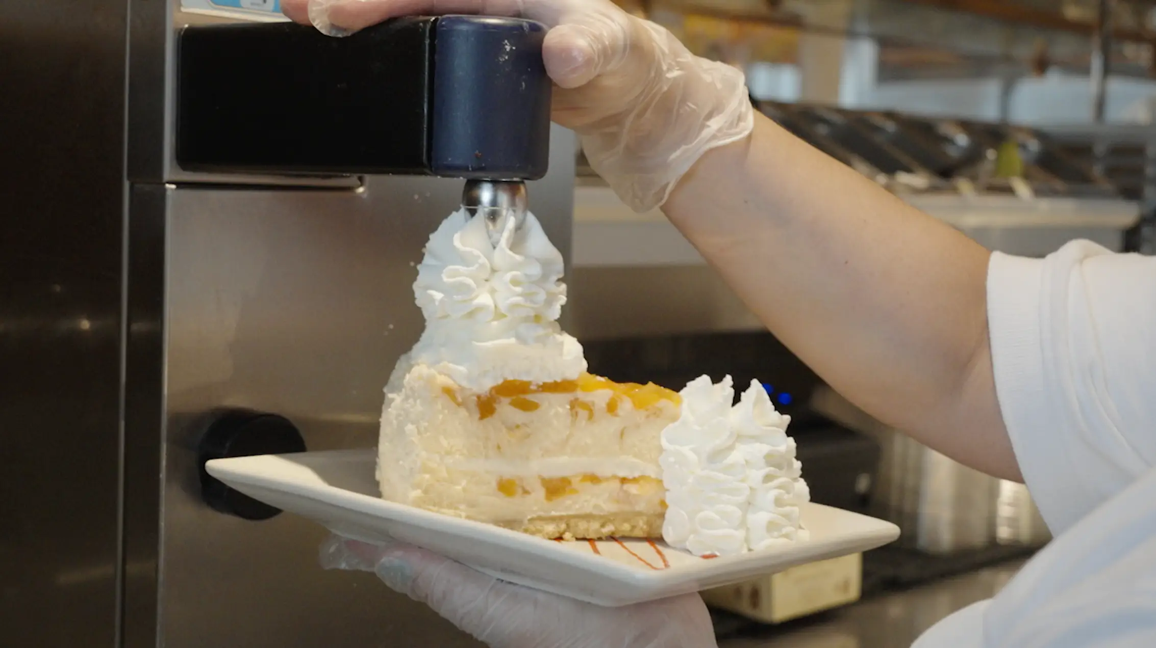 A cheesecake from The Cheesecake Factory getting fresh whipped cream sprayed on top.