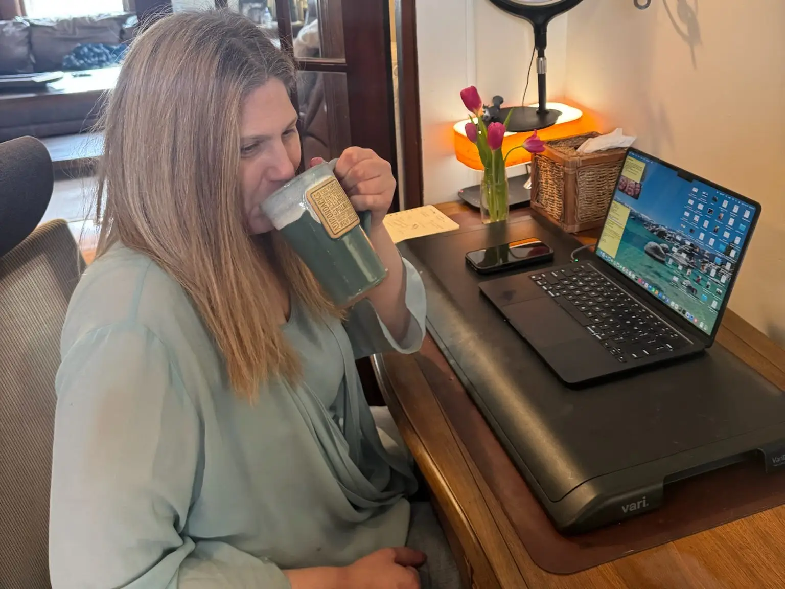 A woman sitting in front of her laptop, drinking from a coffee mug