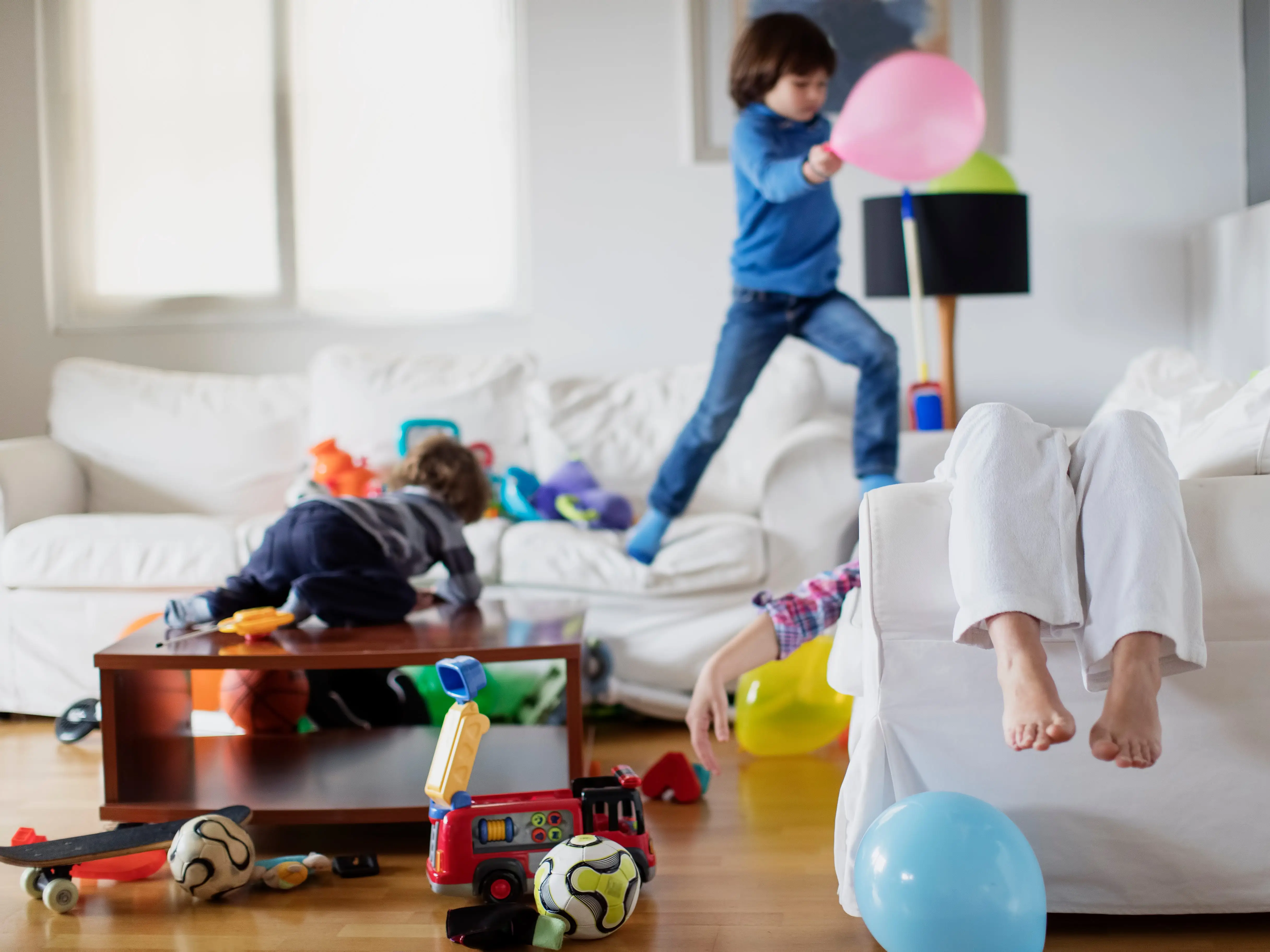 A mother exhausted on the couch while two kids play.