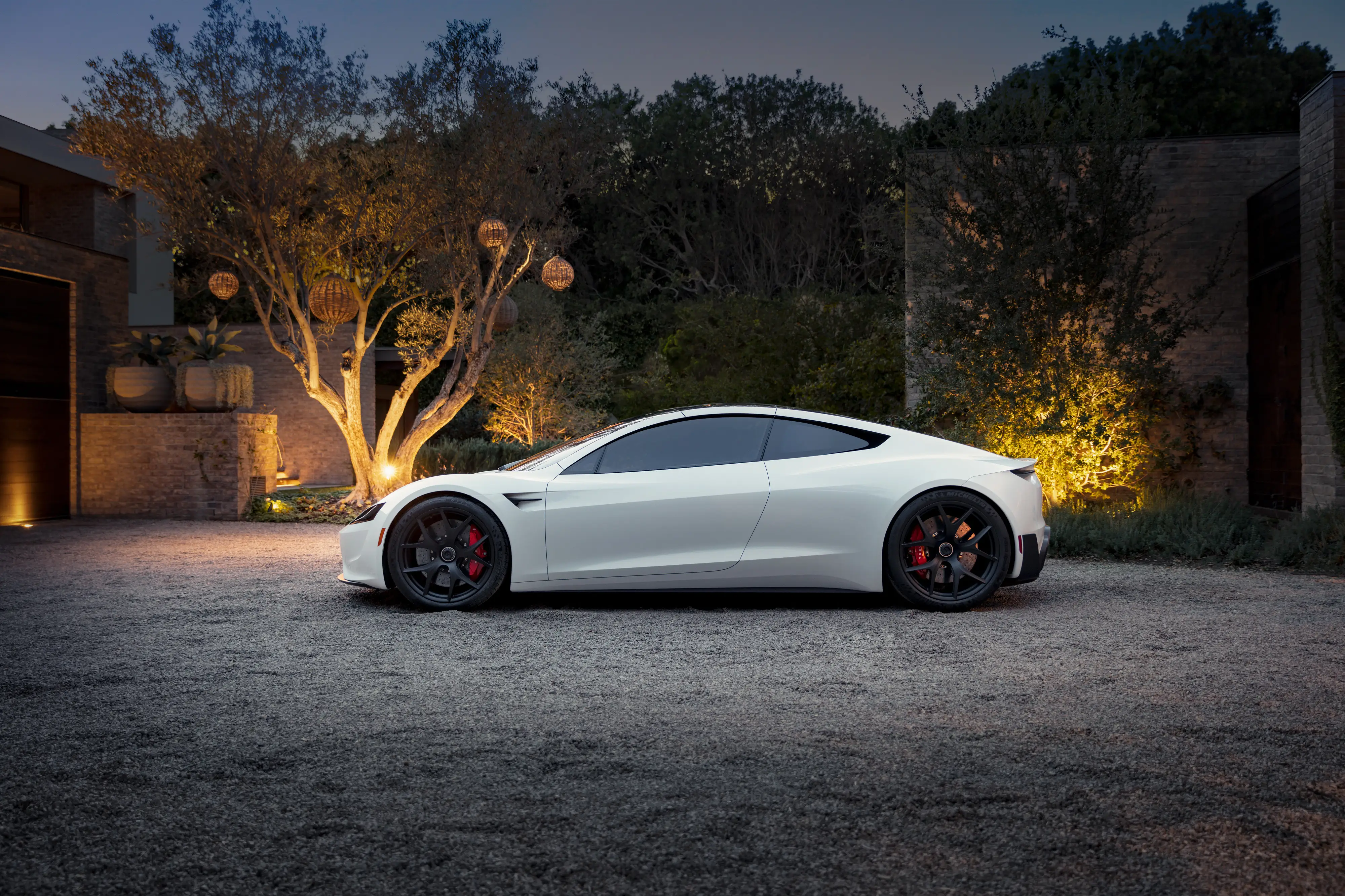 A white Tesla Roadster concept is parked on a gravel driveway.