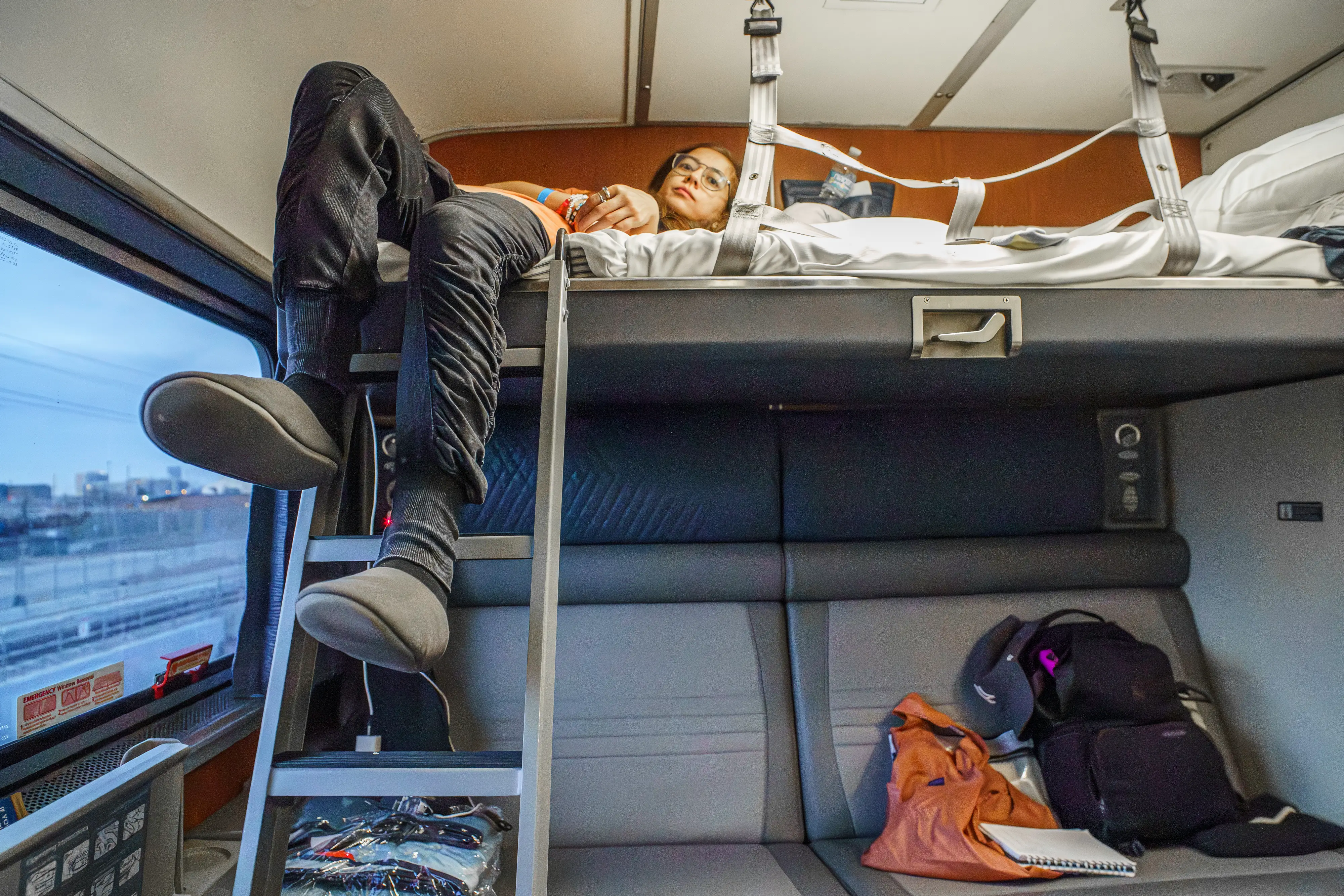 The author lays in the top bunk of an Amtrak bedroom with her legs hanging over the ladder