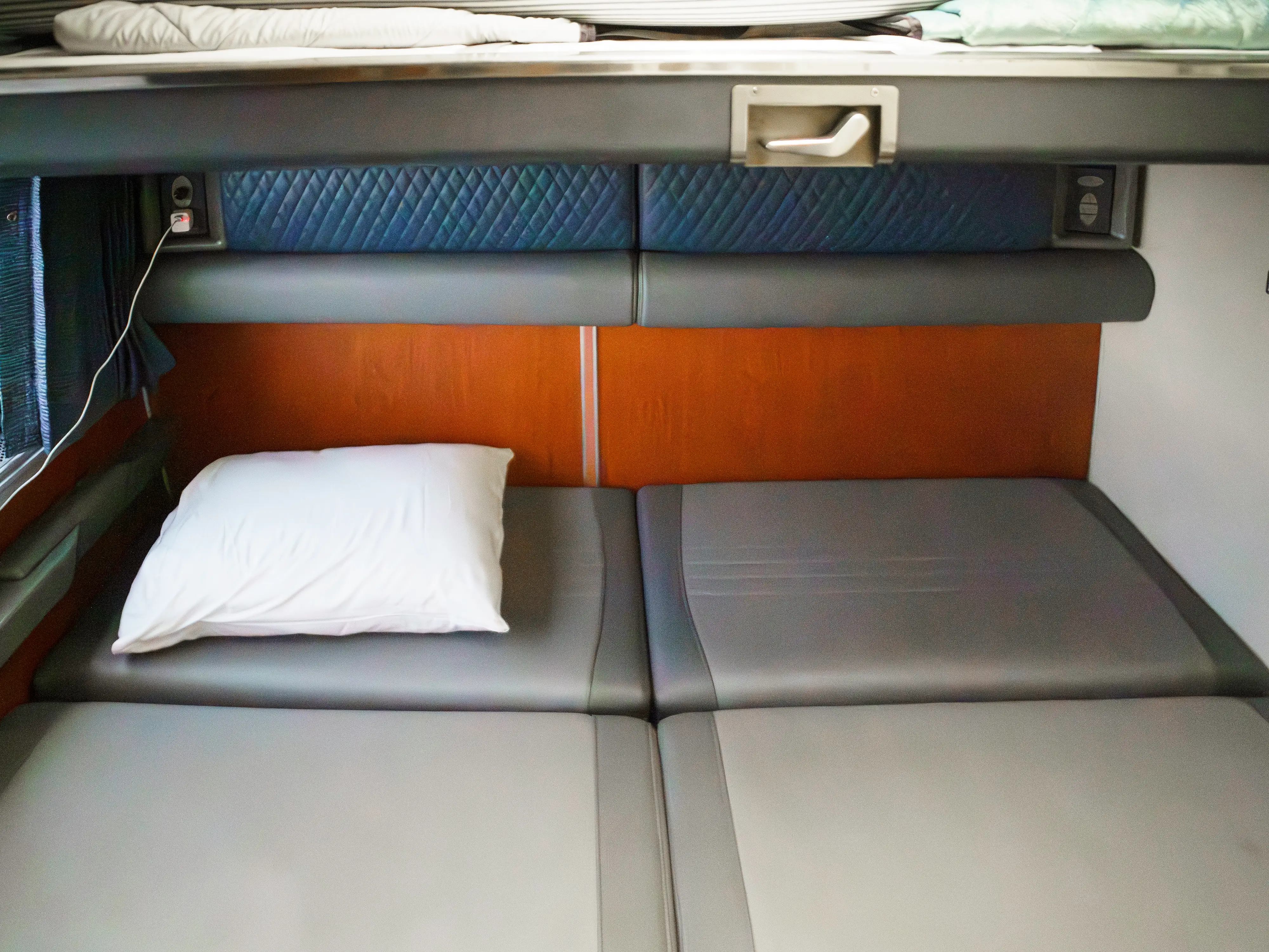 An Amtrak couch pulled out into a bed with a pillow in the top left corner