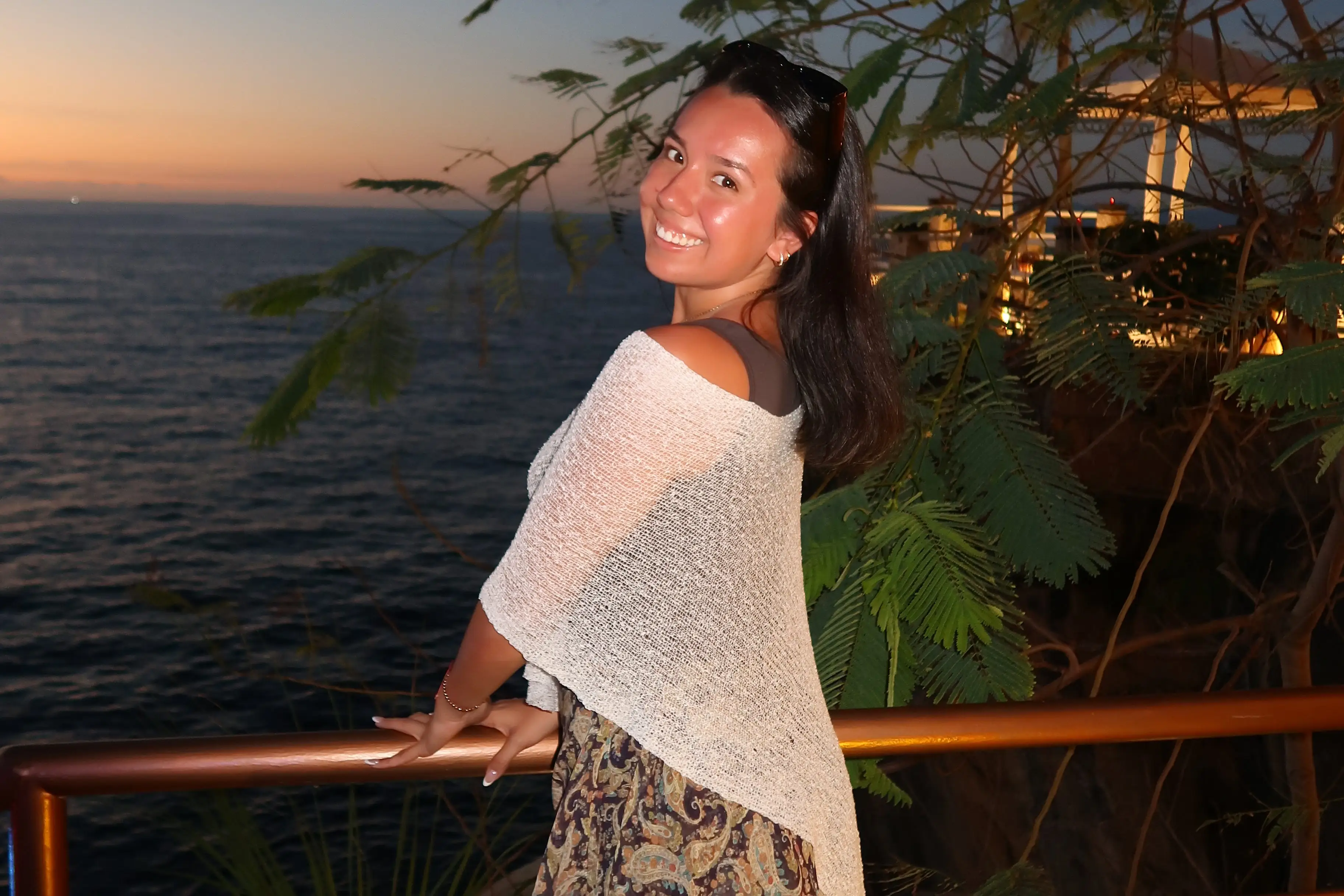 A young woman smiles while holding a railing, overlooking a large body of water.