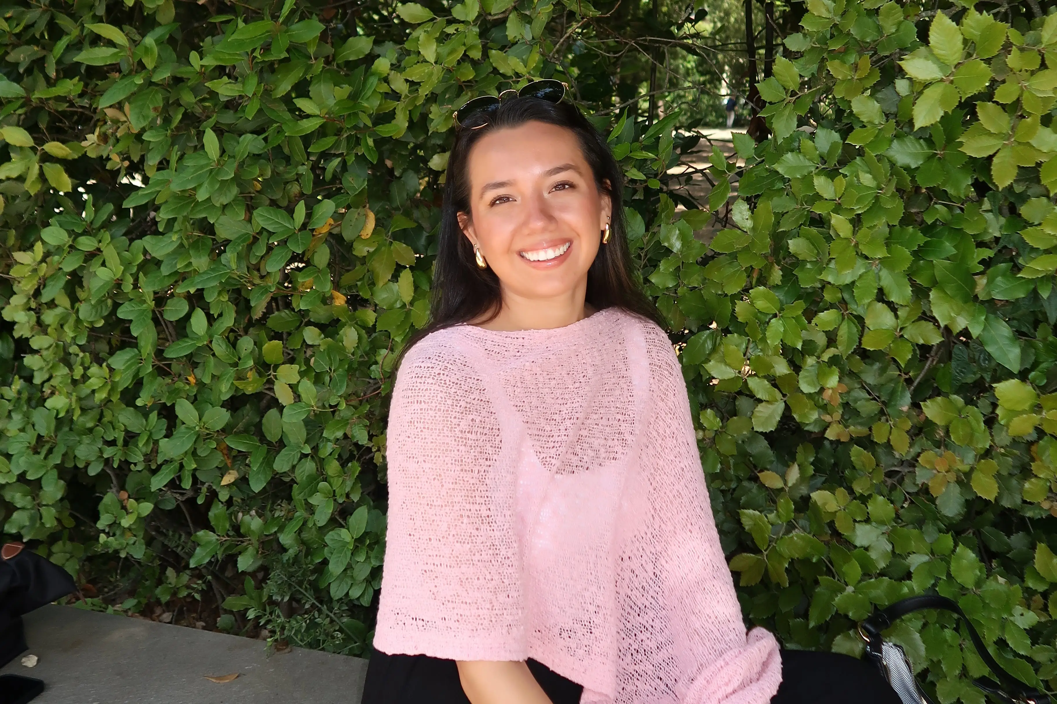 A woman in a pink pancho sits under a tall bush.