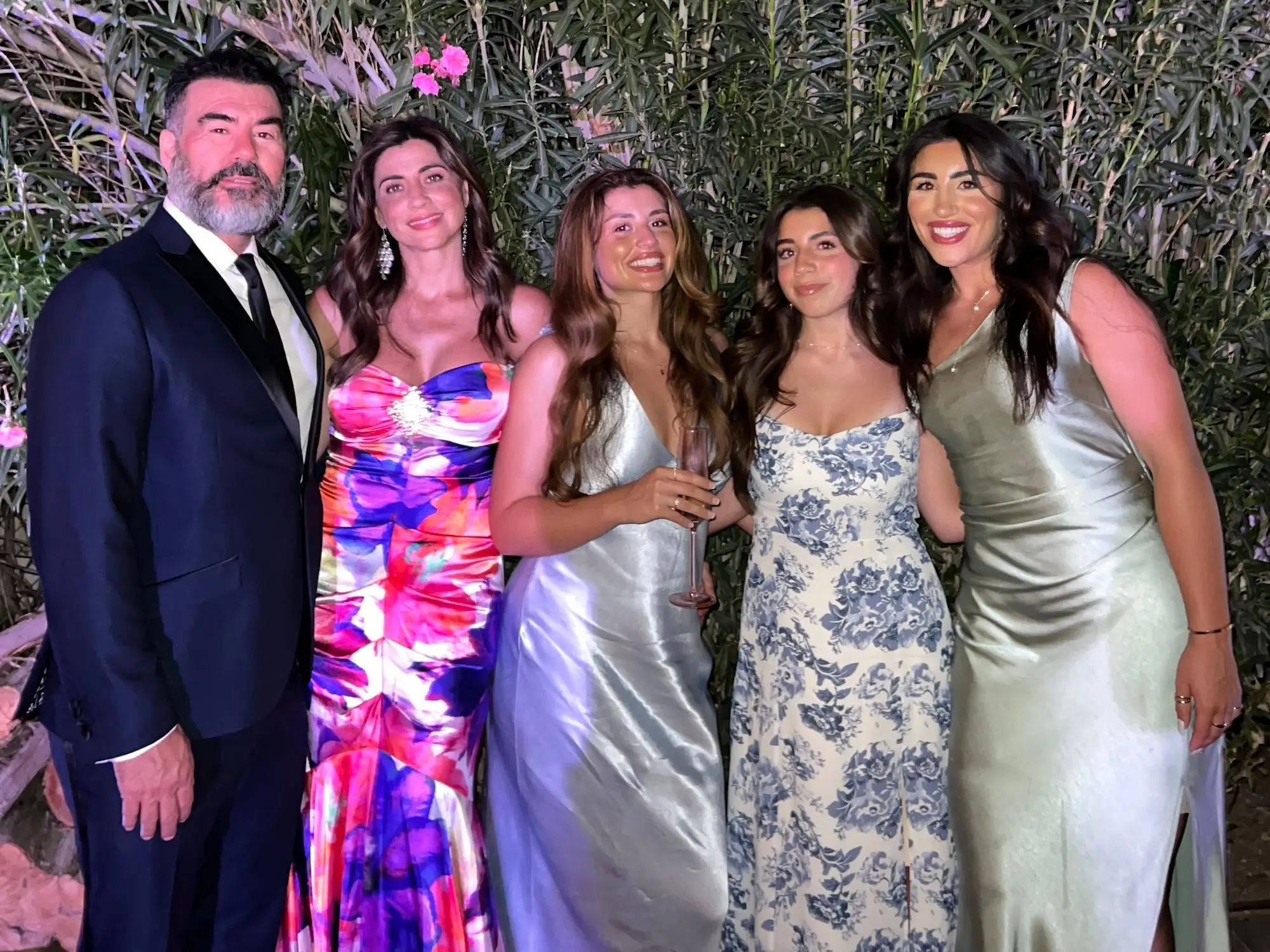 A family smiles in front of greenery in fancy clothing.