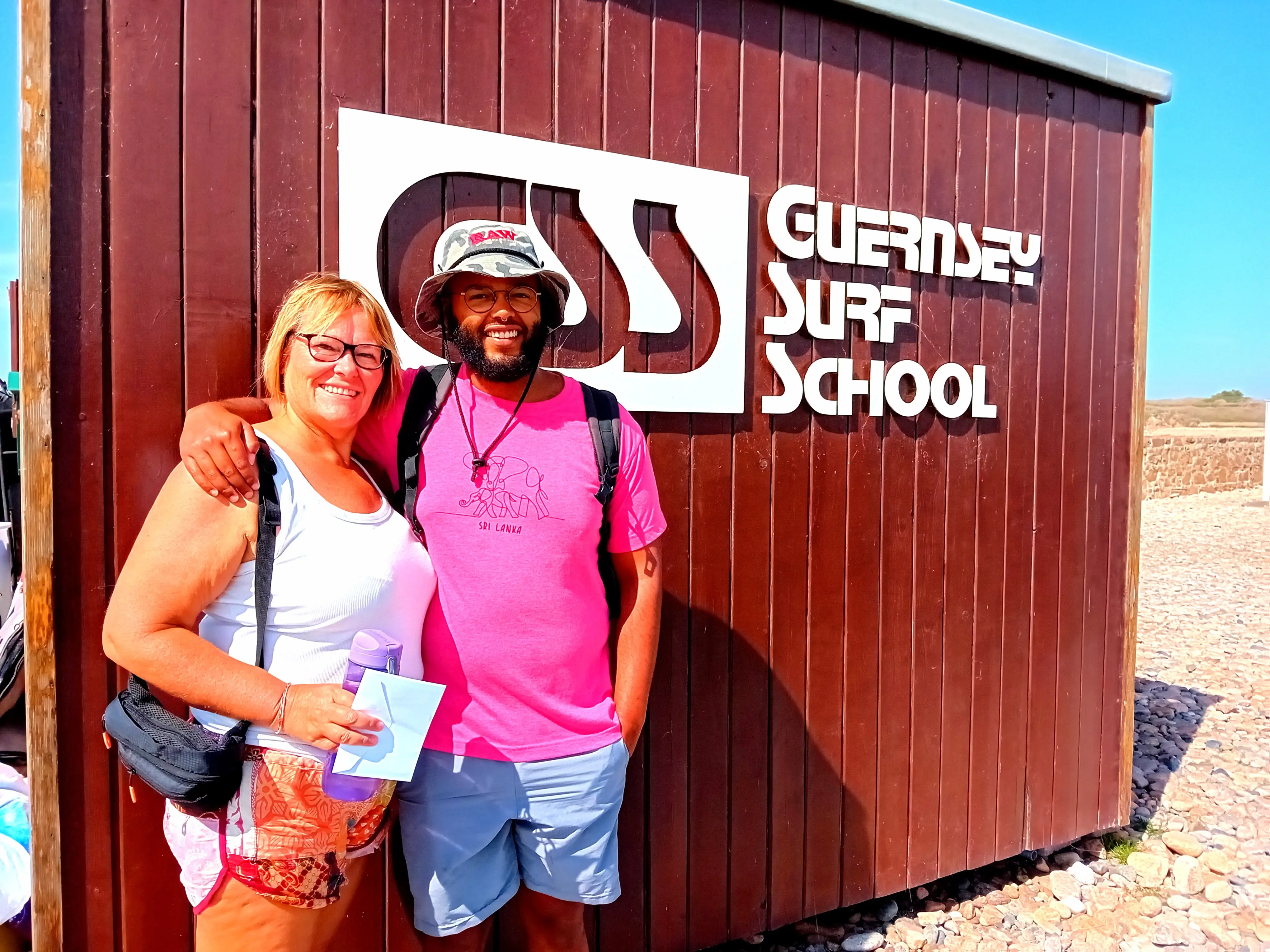 A woman and her son posing in front of Guernsey Surf School.
