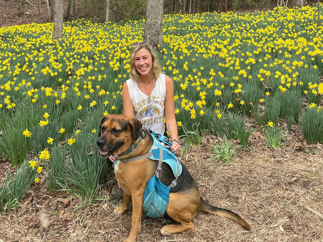Mikala sits in a field of yellow flowers with her dog.