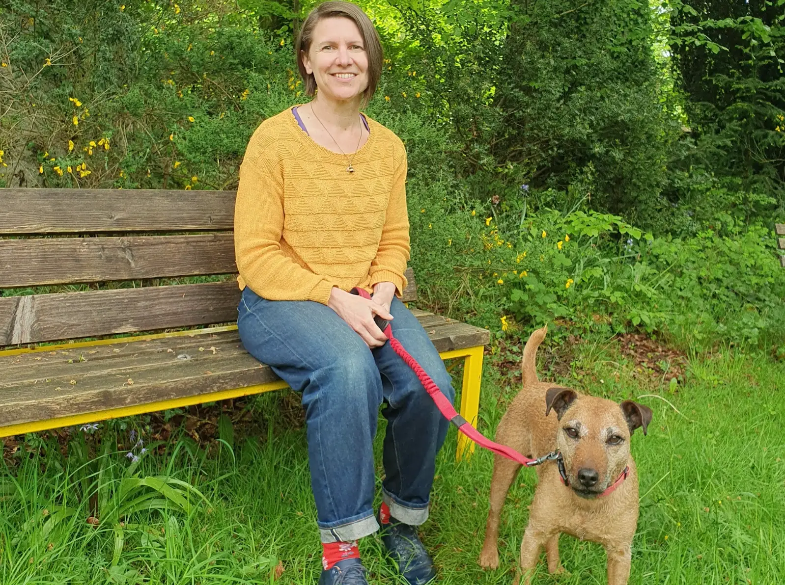 The writer sitting on a bench with her dog, surrounded by greenery.