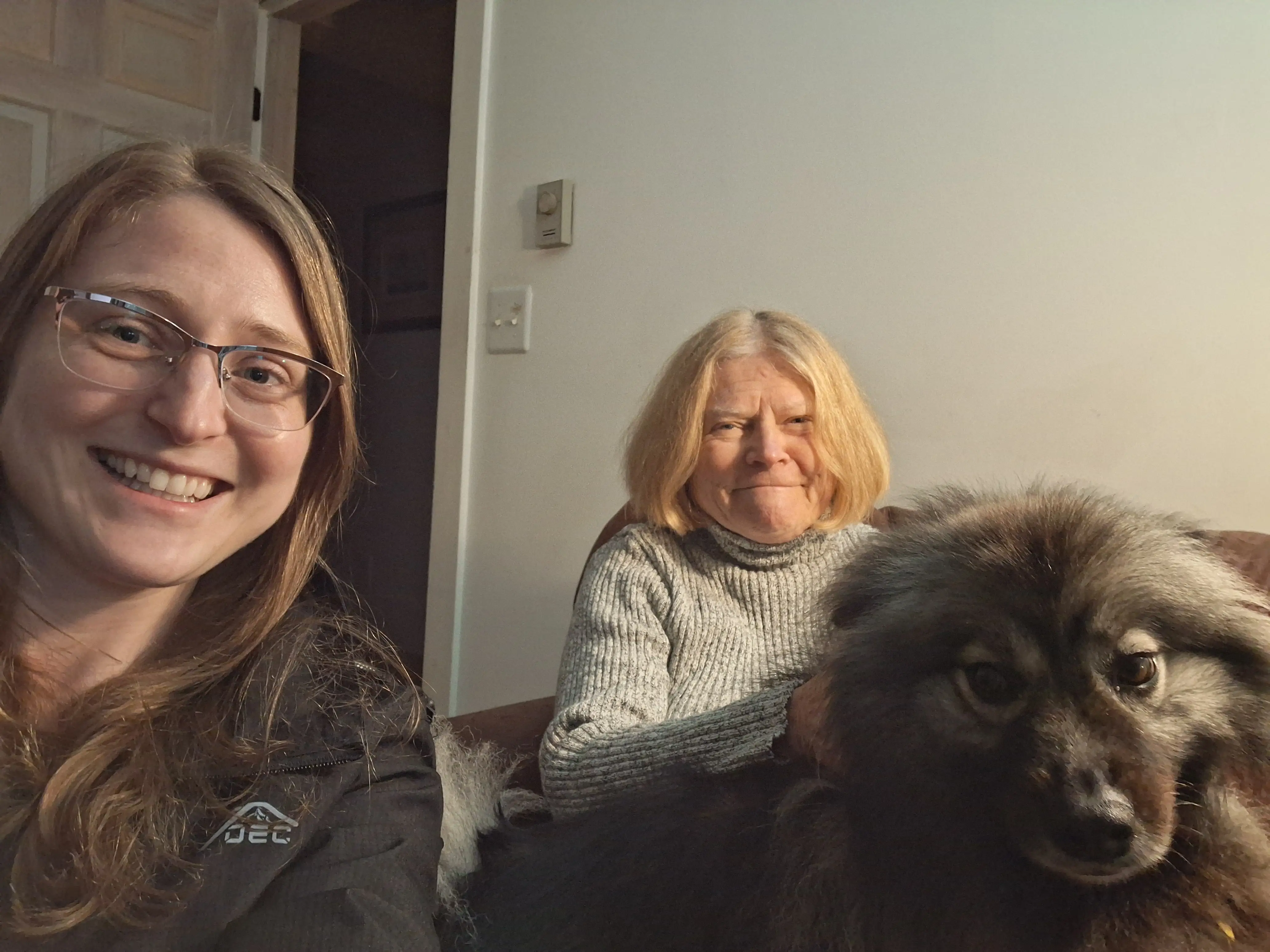 A younger and older woman sitting on a sofa with a dog.