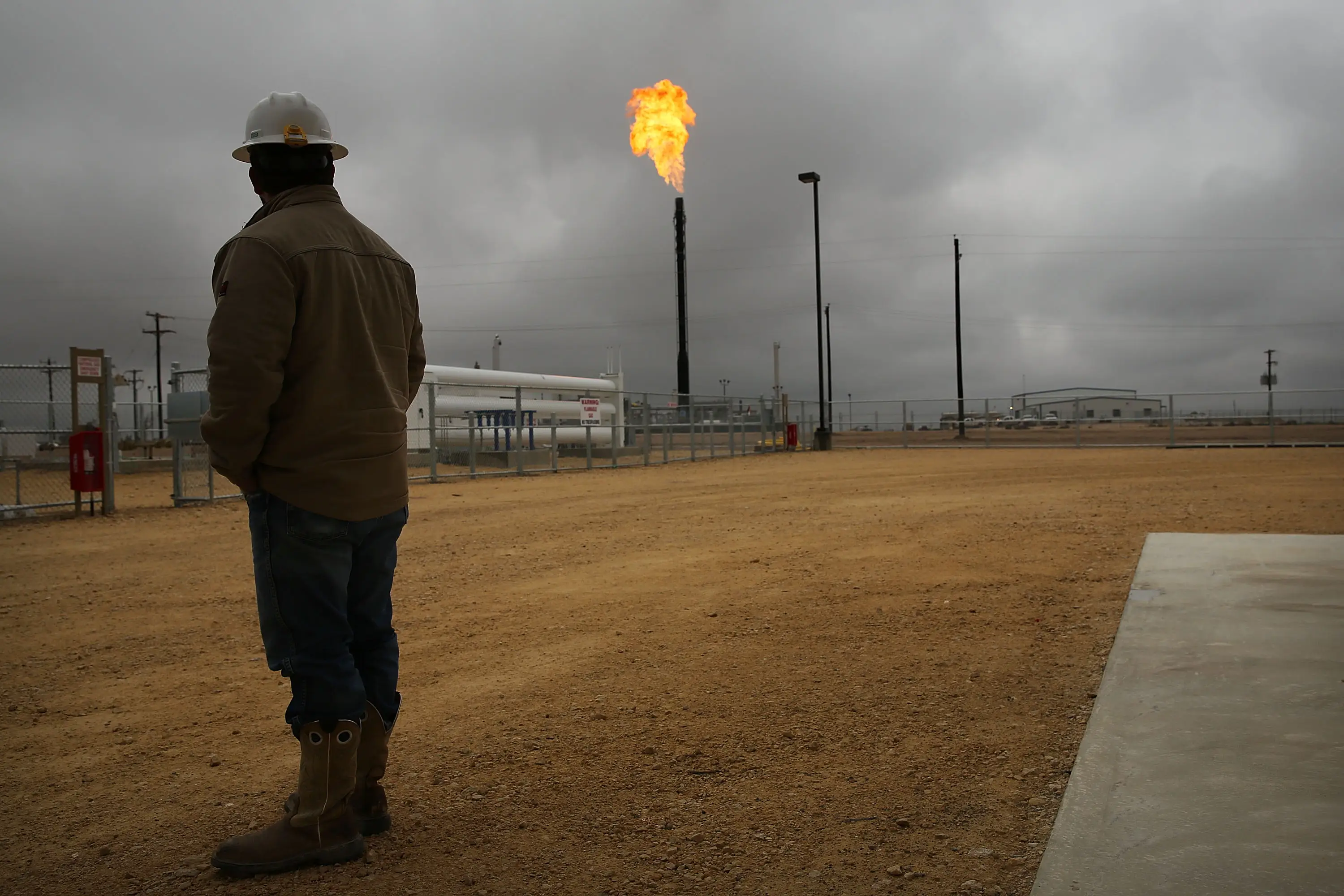 A man stands in front of a natural gas plant that's flaring in Texas
