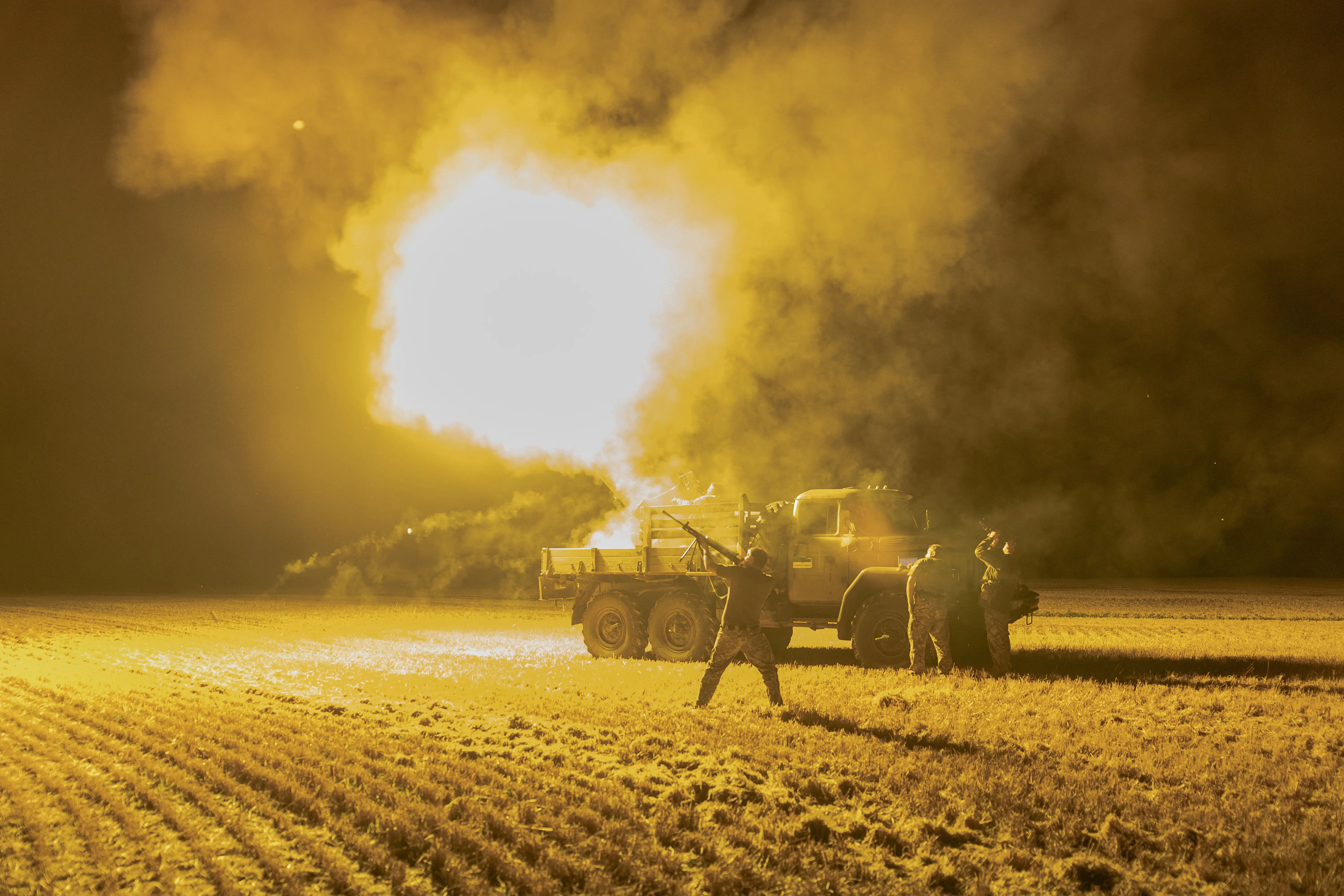 Orange smoke is lit up orange as a figure fires a gun in the air in a field at night time
