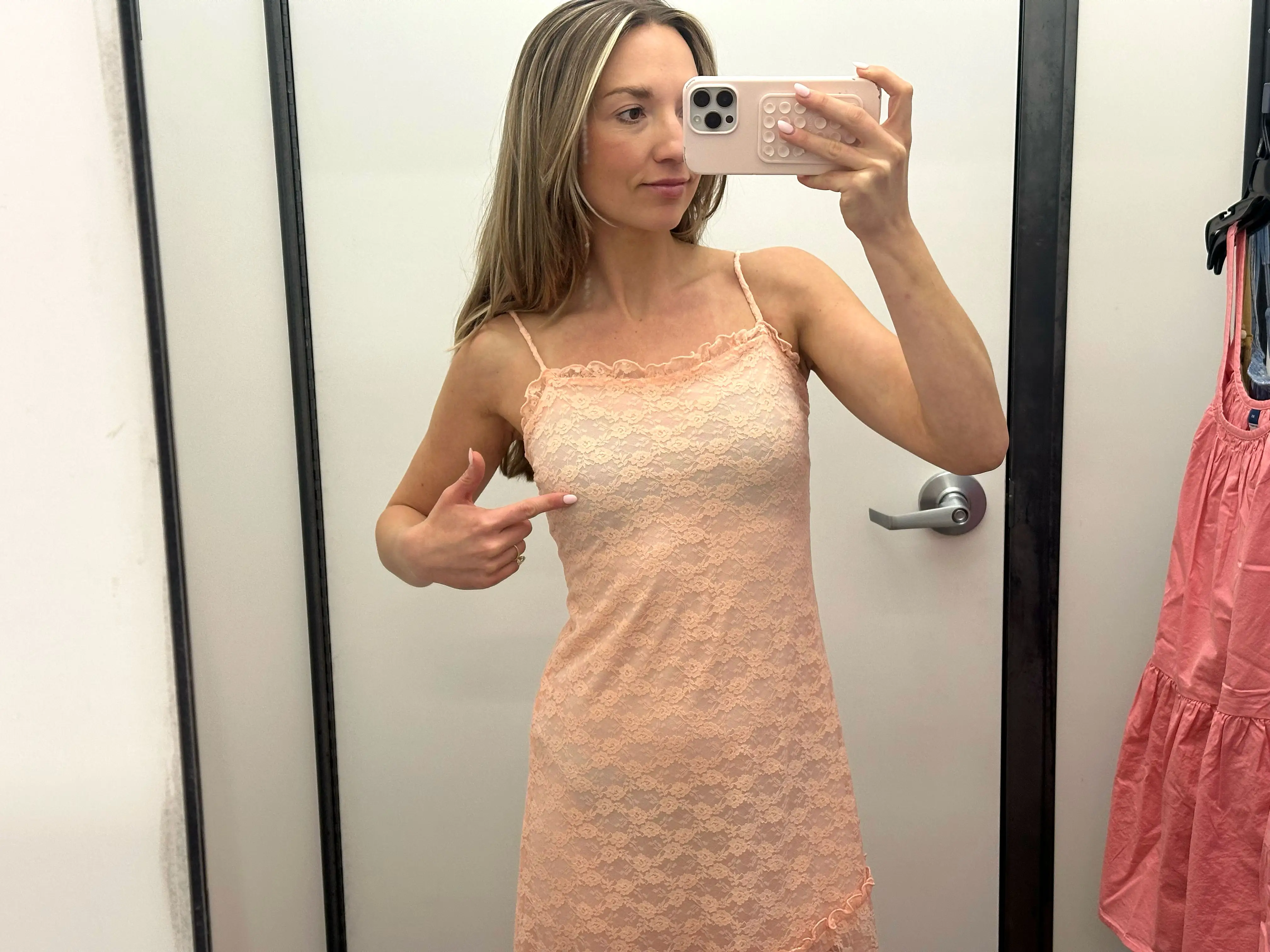Chloe wears a peach lace midi dress and points to her chest.