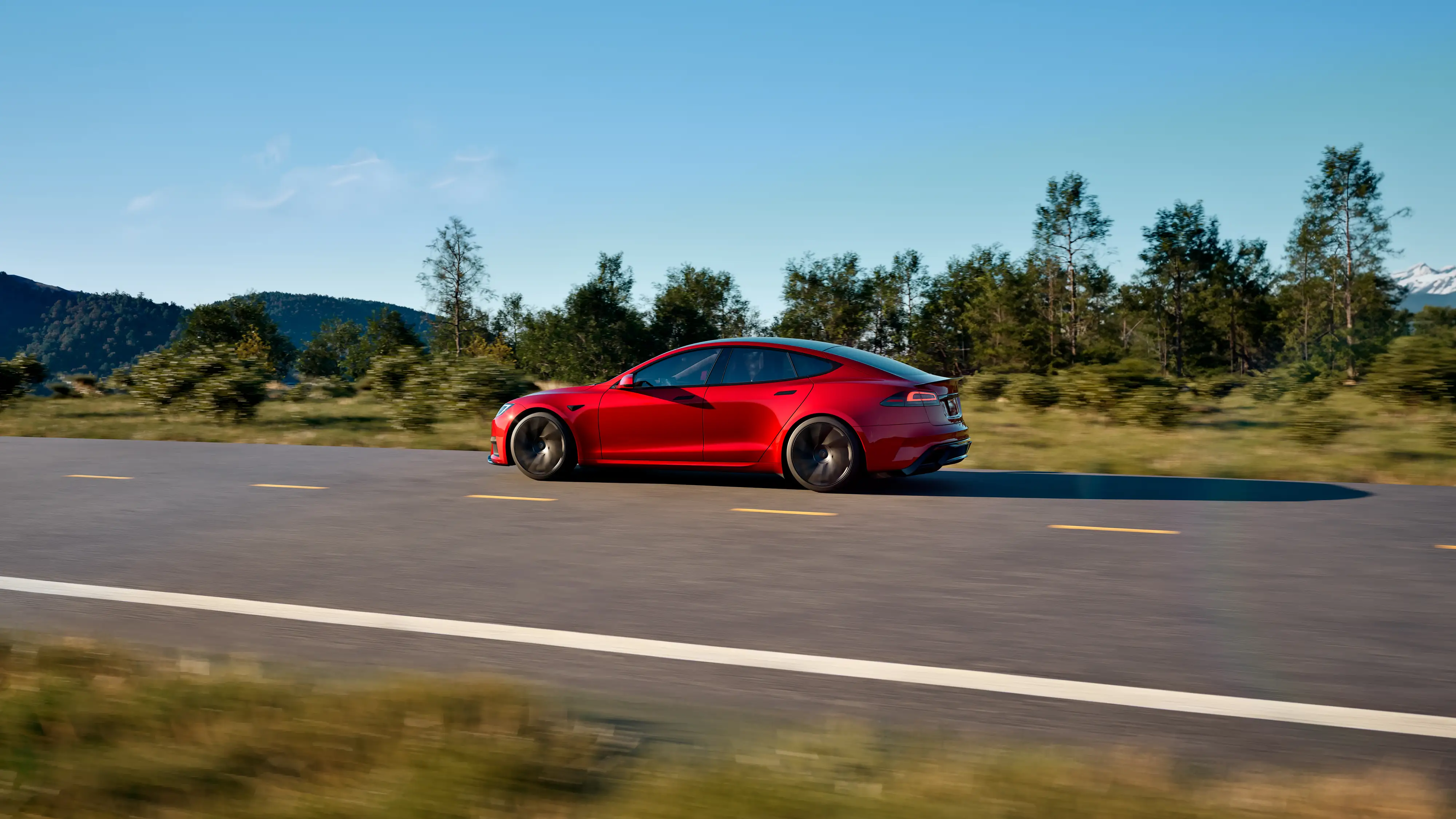 A red Tesla Model S drives past trees on a two-lane road.