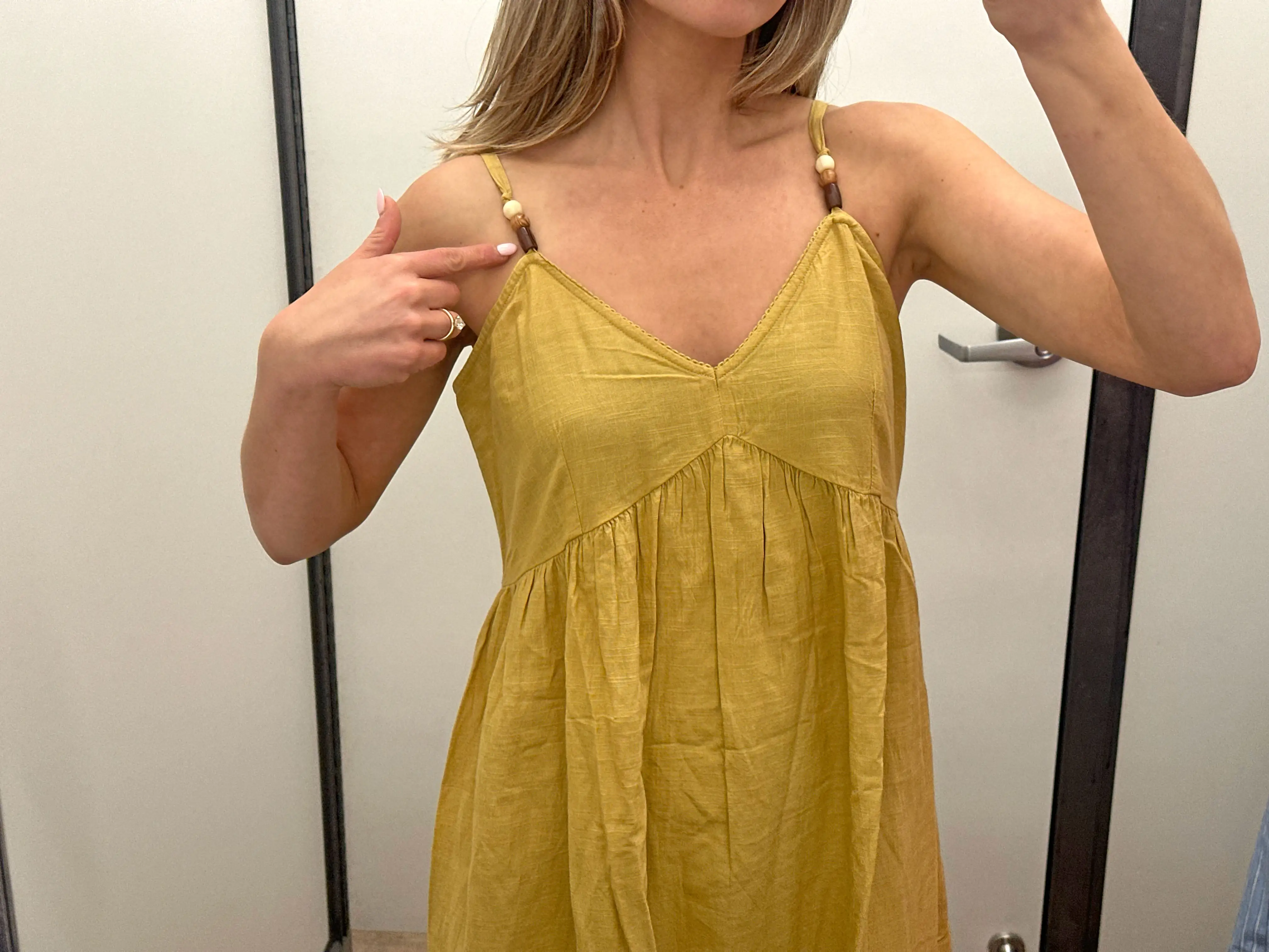 A close-up of Chloe wearing a yellow midi dress and pointing to the beaded straps.