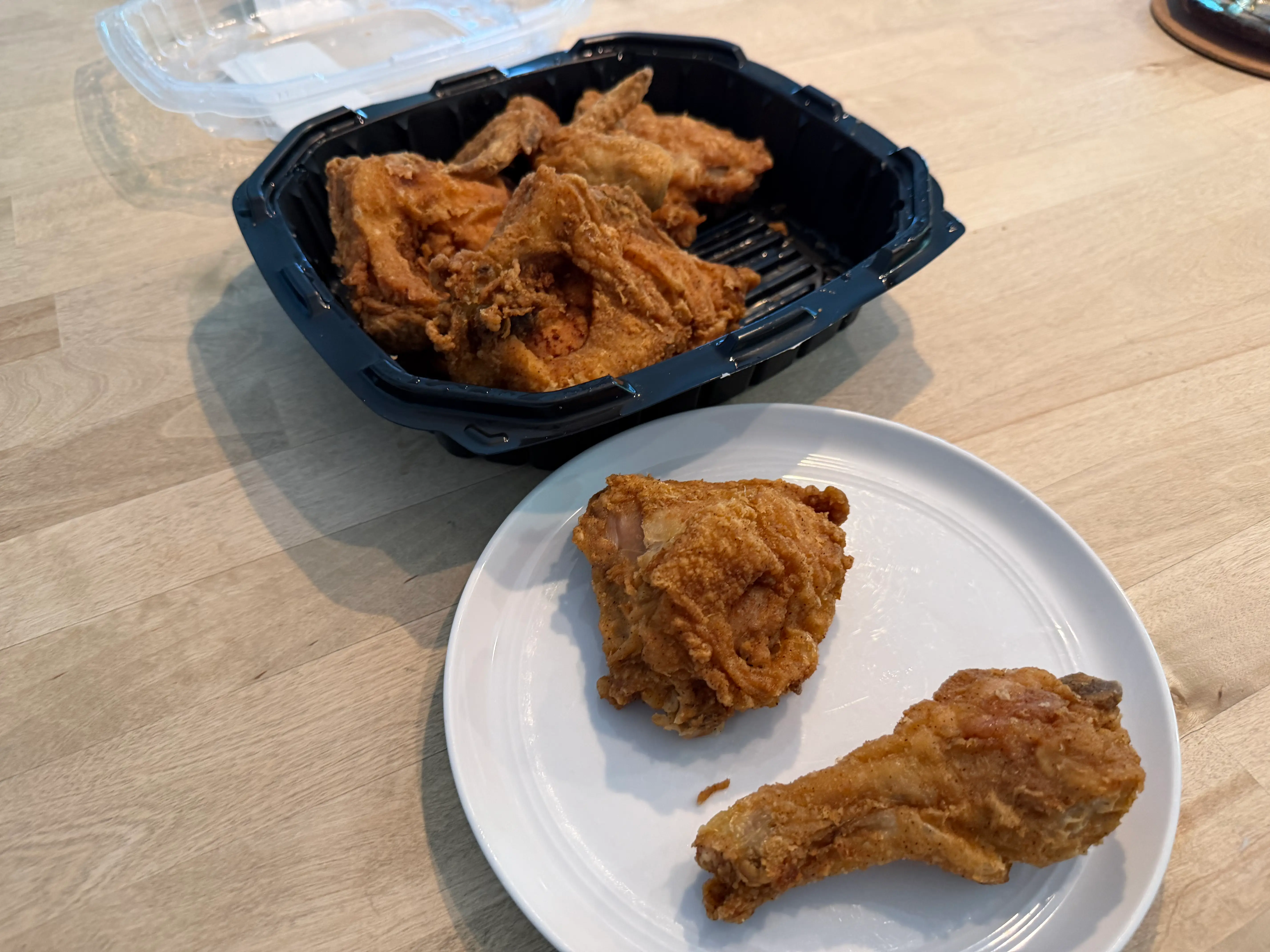 Two pieces of fried chicken on plate in front of container of fried chicken from Shop Rite