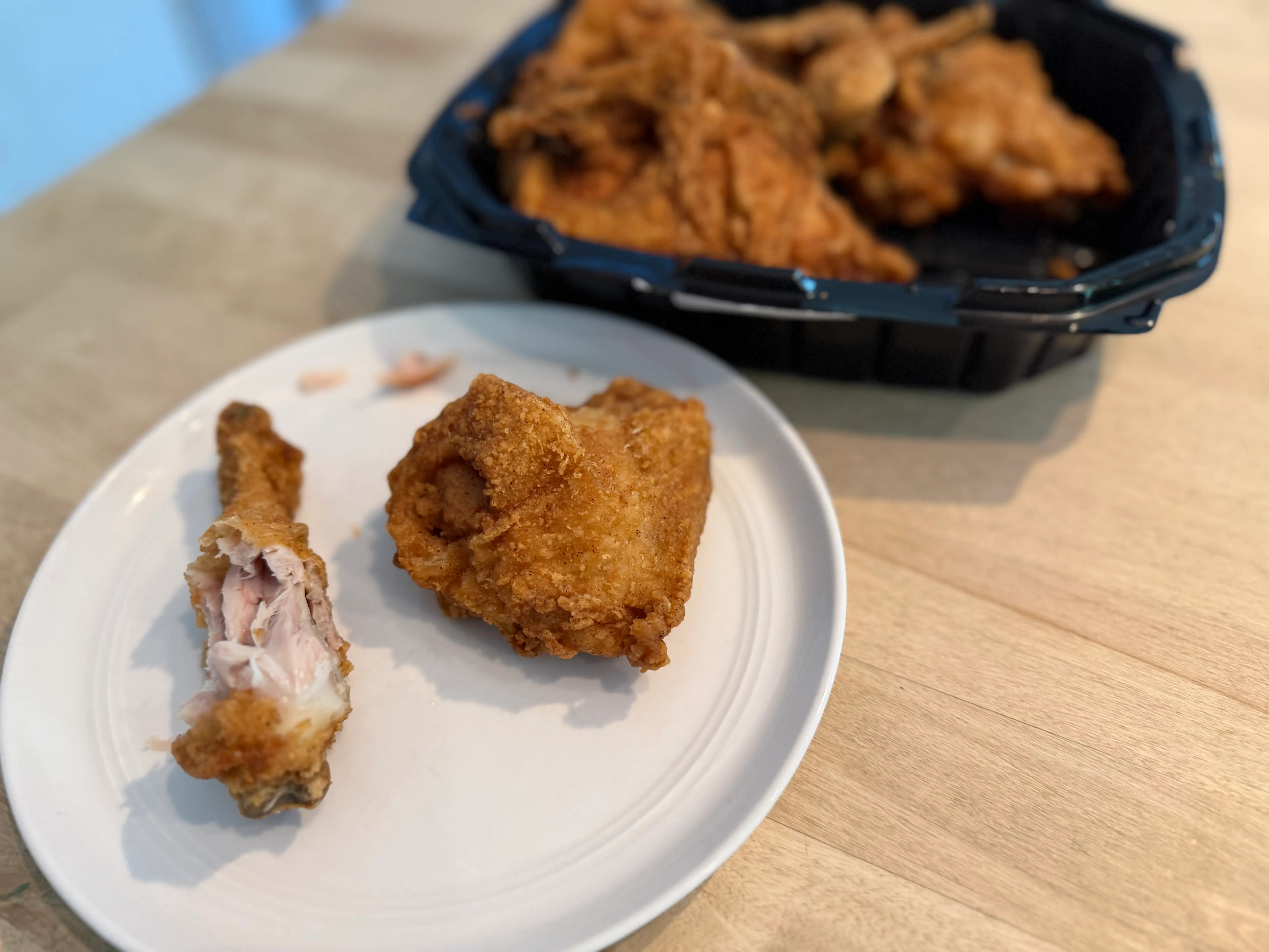 Two pieces of Shop Rite fried chicken on plate, one with skin removed partially with container of chicken in background