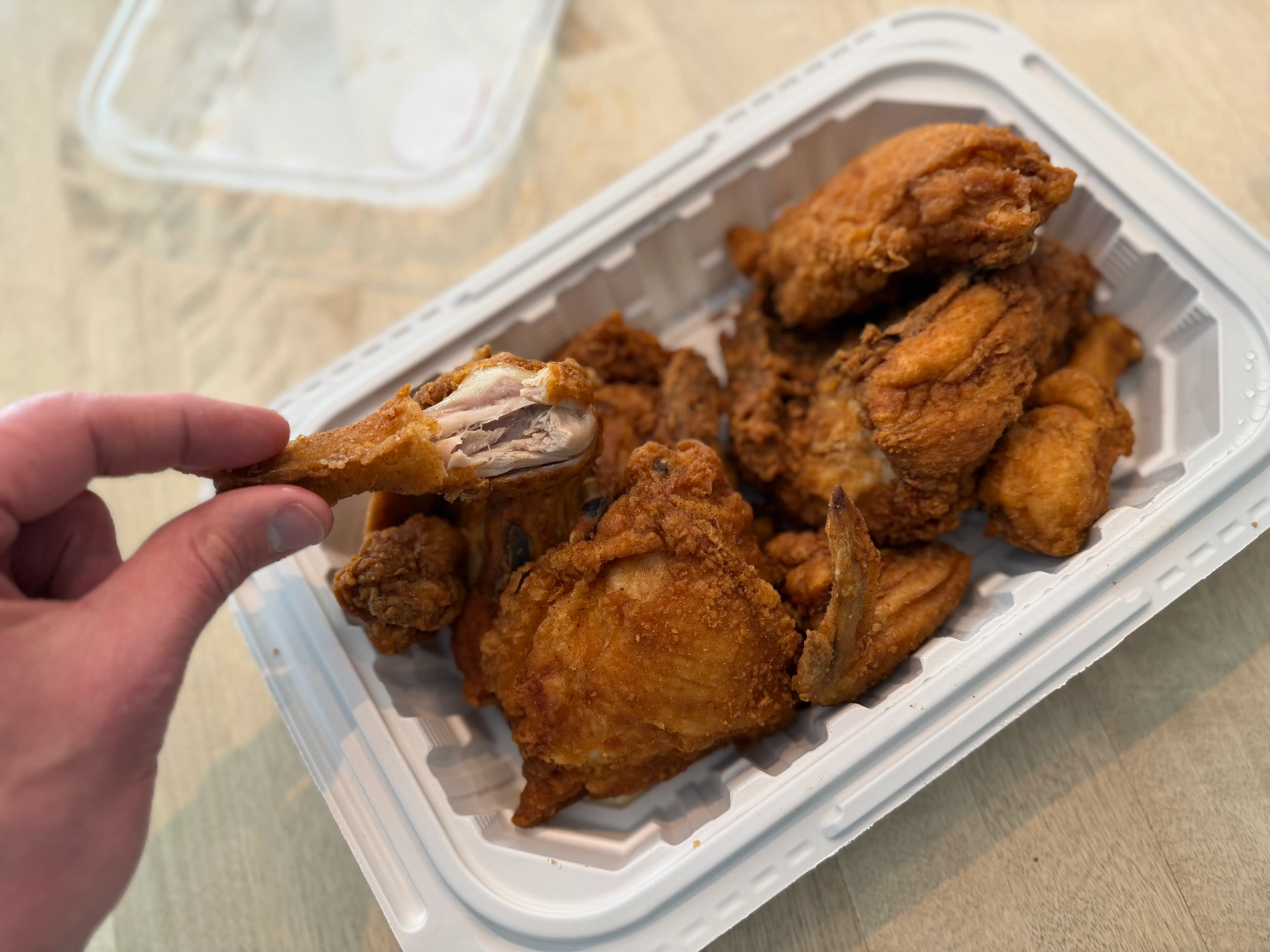 Hand holding a piece of fried chicken from Stop & Shop above a container of chicken