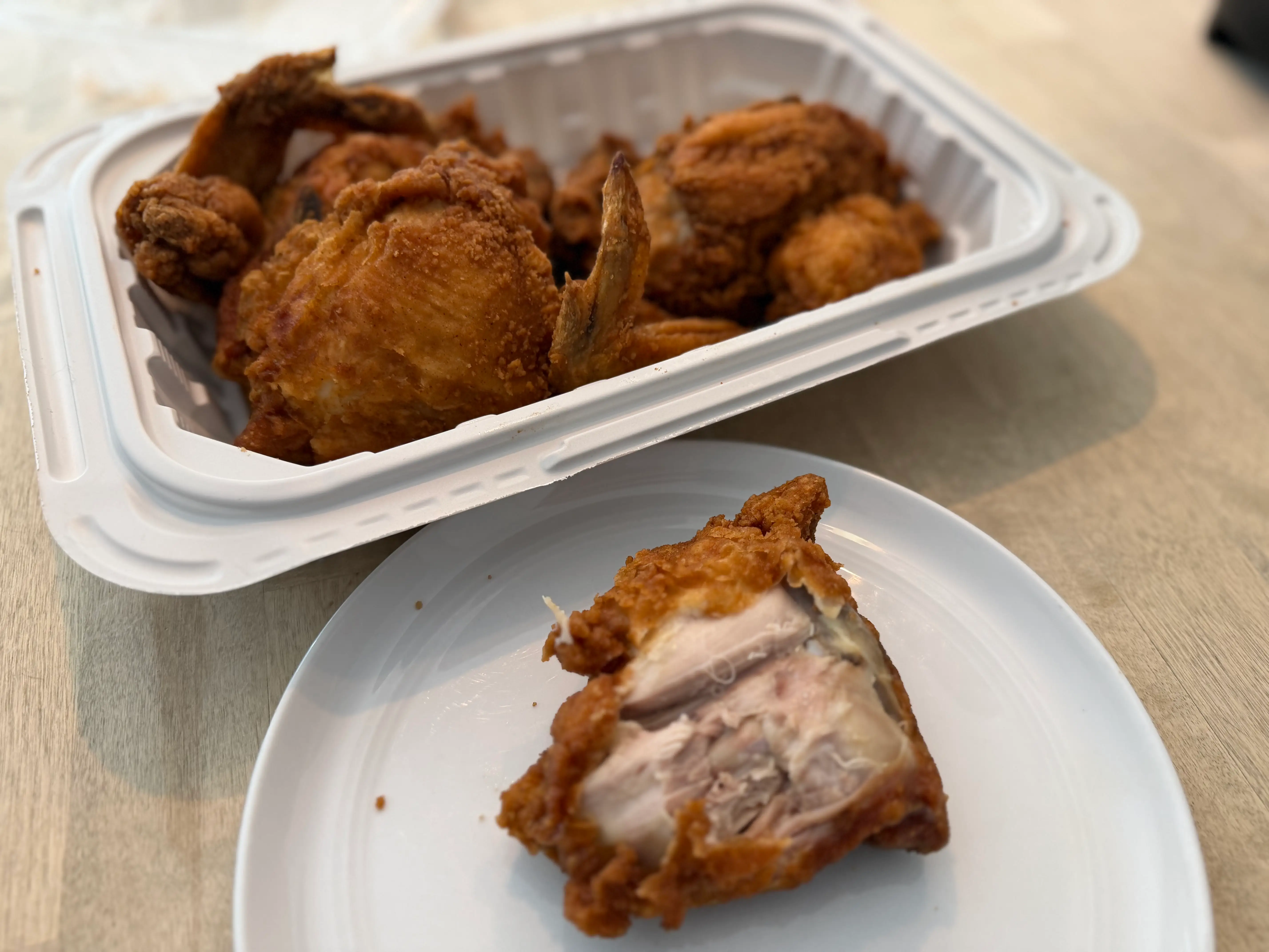 Piece of fried chicken from Stop & Shop on plate with skin peeled off with container of chicken behind it