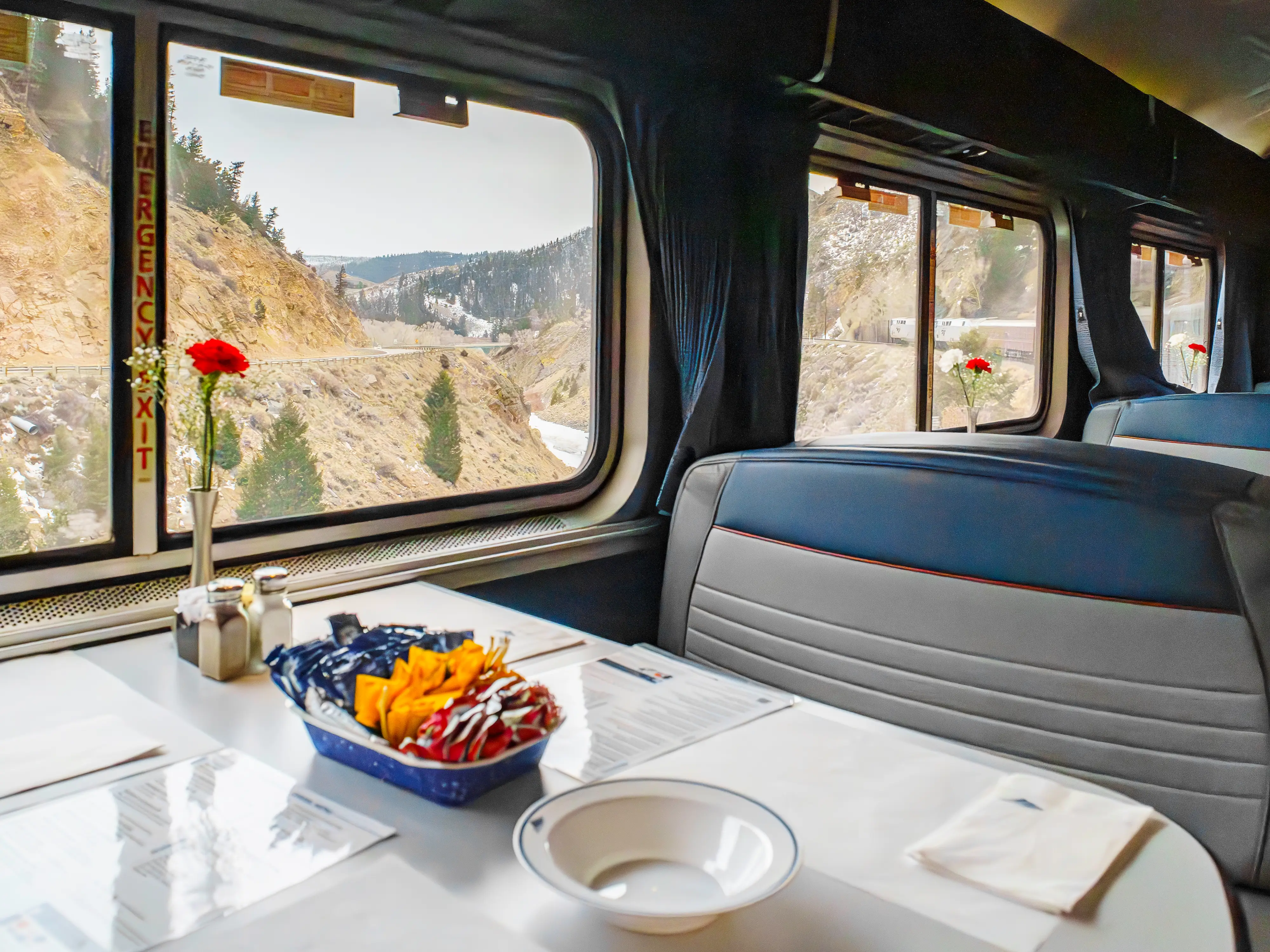 Empty Amtrak dining tables in front of windows showing mountains outside