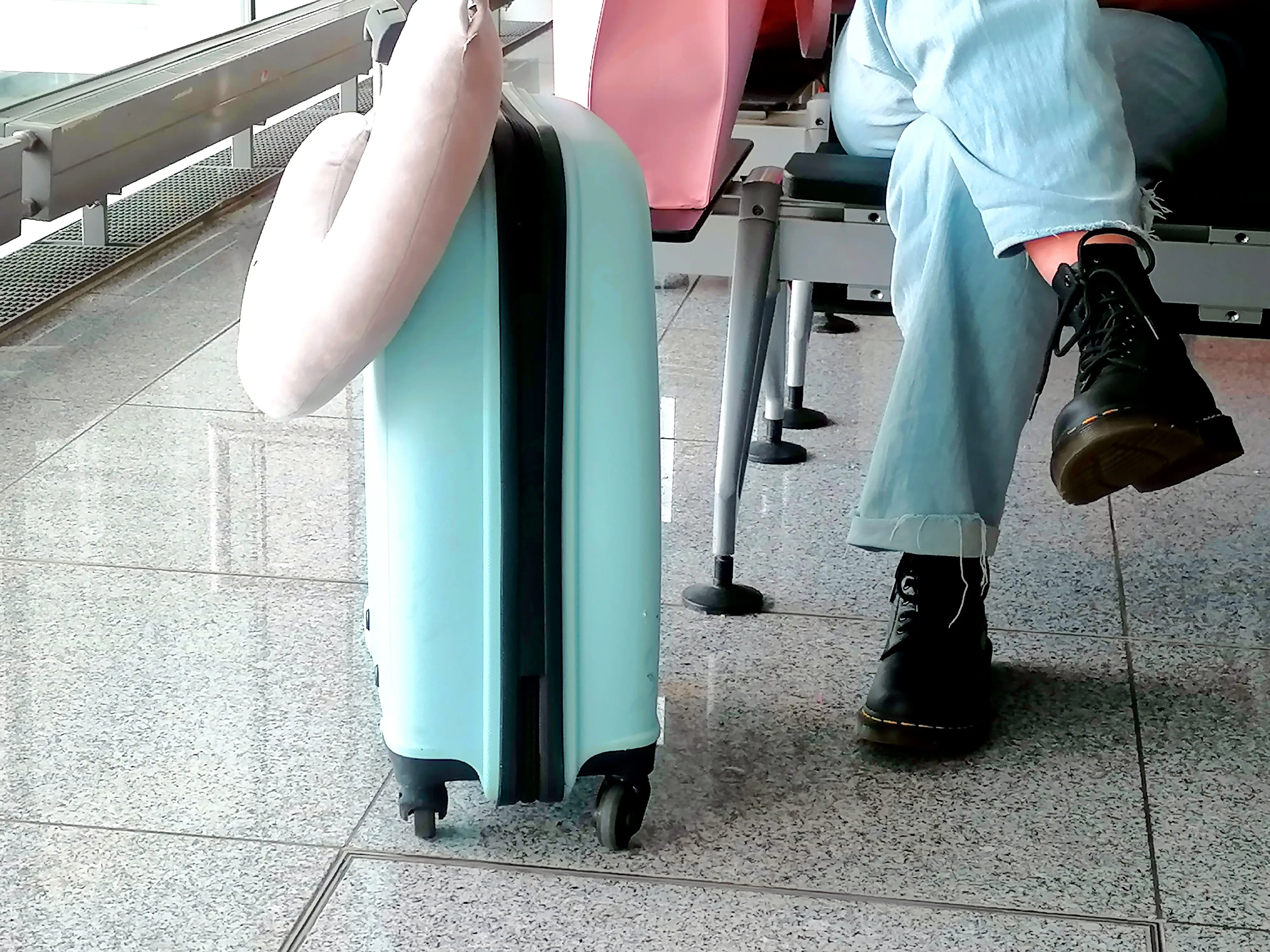 Suitcase with neck pillow on it next to person sitting in airport