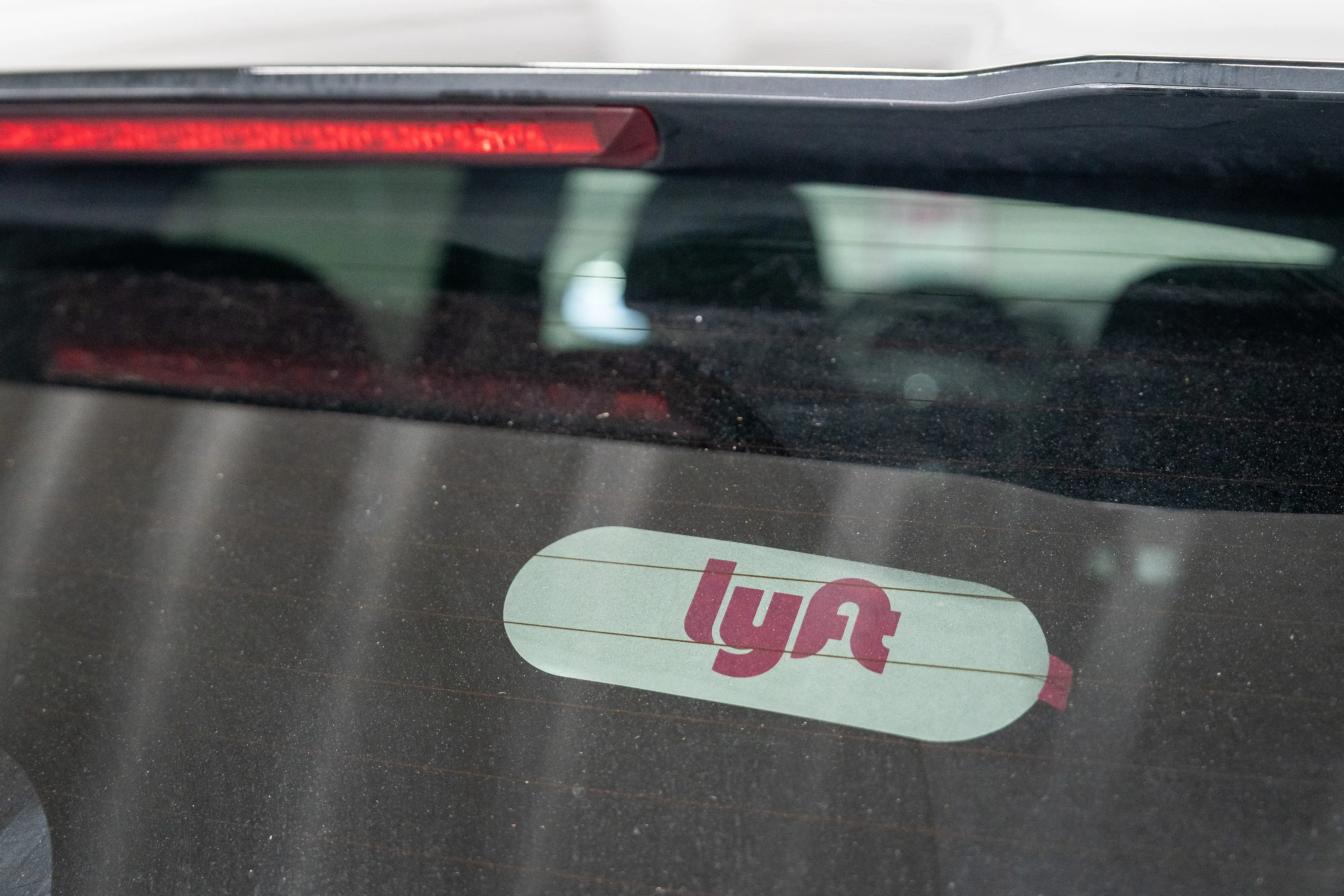 A white-and-pink Lyft sticker sits on the inside of a car's rear windshield.