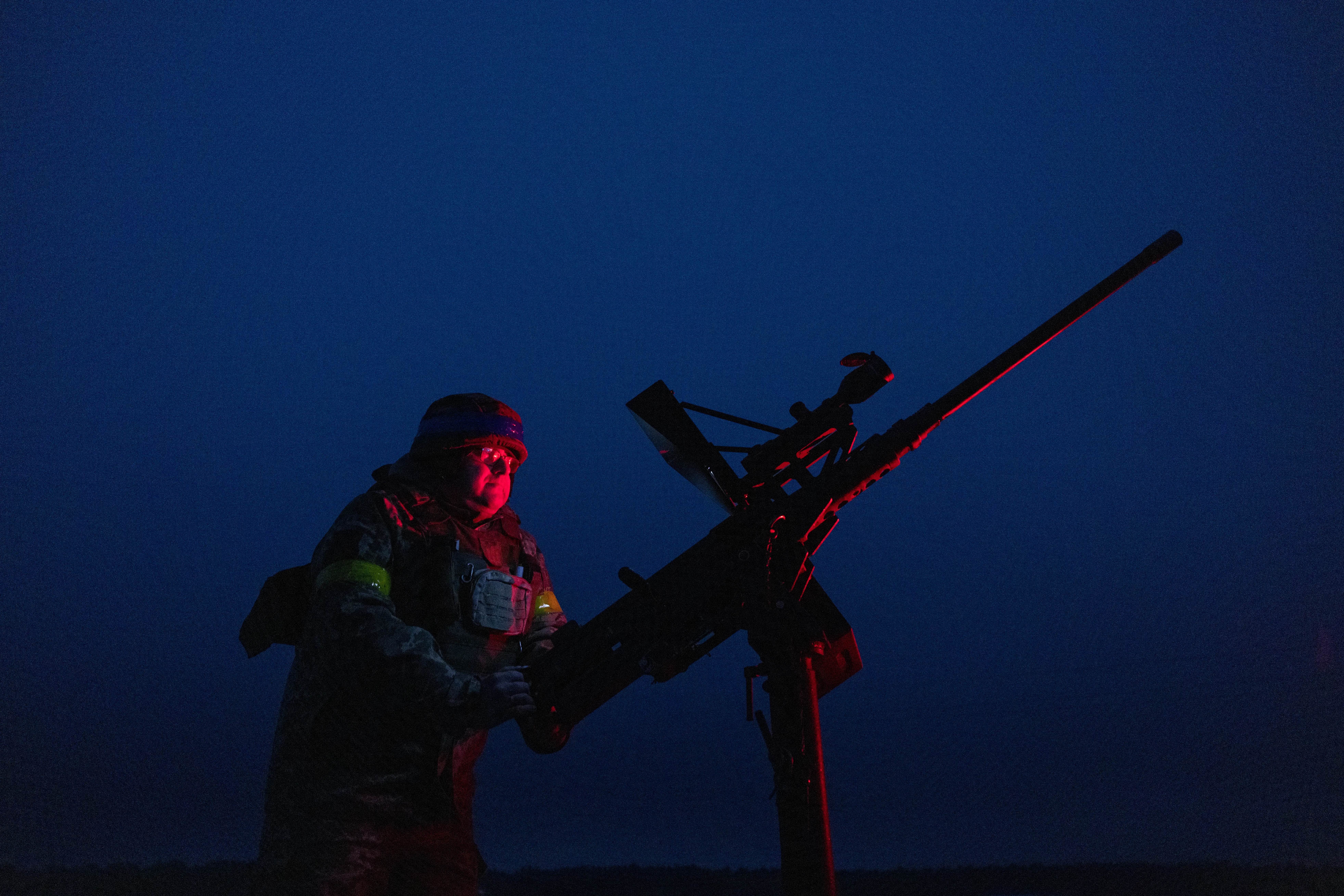A man stands beside a large weapon against a night sky lit up by red light