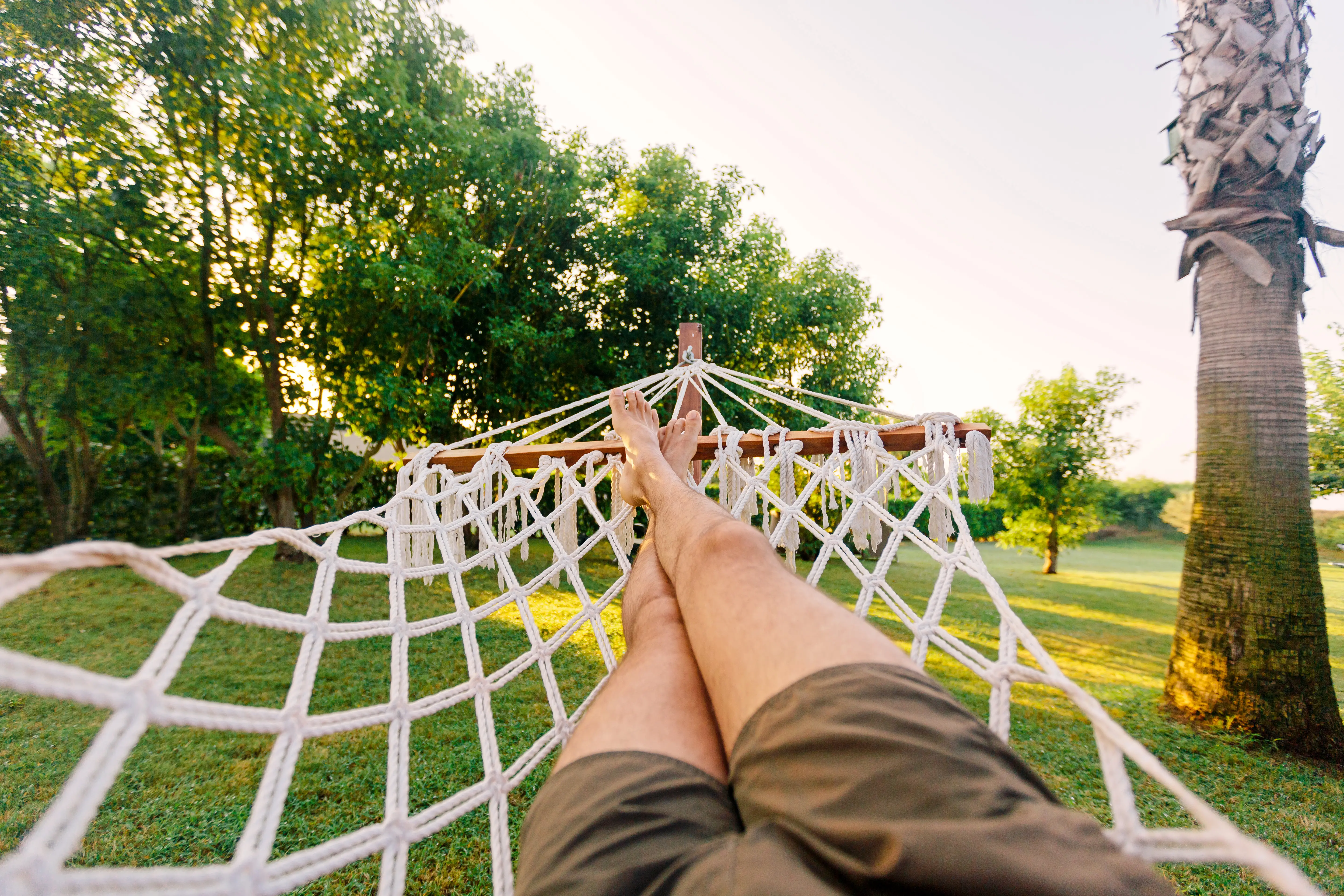 A person wearing shorts lounges on a hammock.