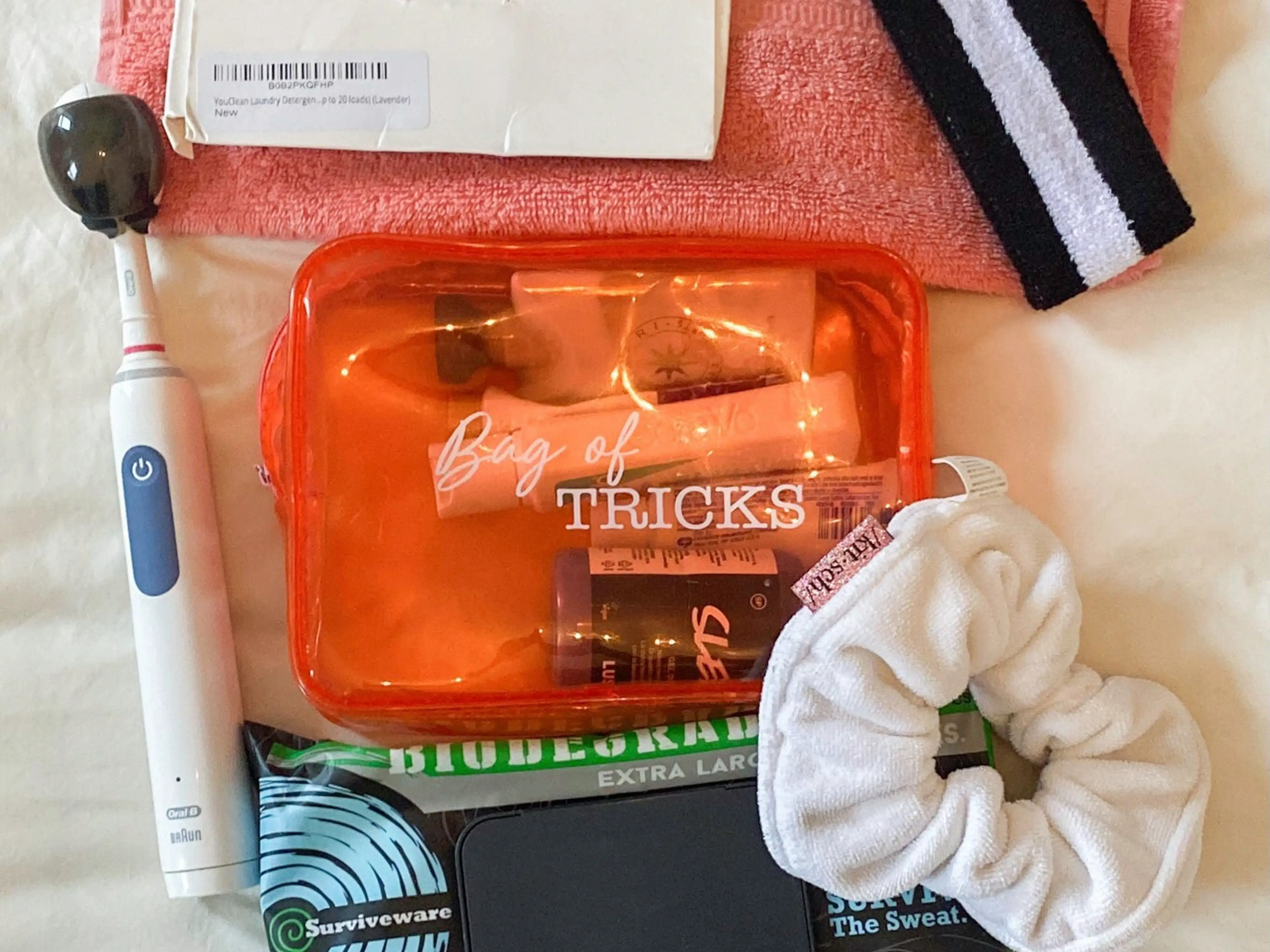 A white background with a black packagee of body wipes, a white scrunchy, a white electric toothbrush, a pink rag, a black and white striped sweatband, and a white package of laundry sheets.