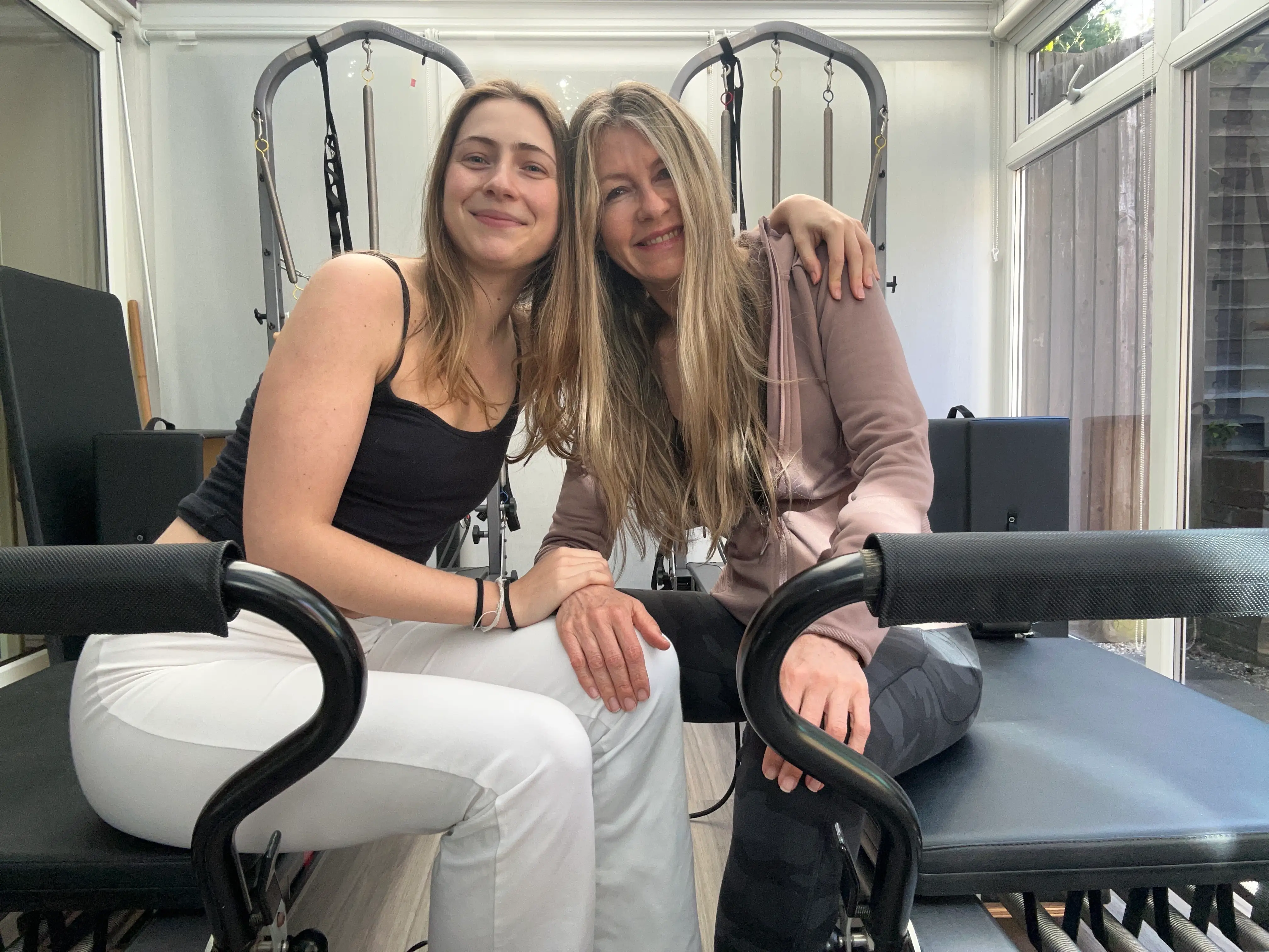 A mother and her daughter sitting on Pilates reformers.