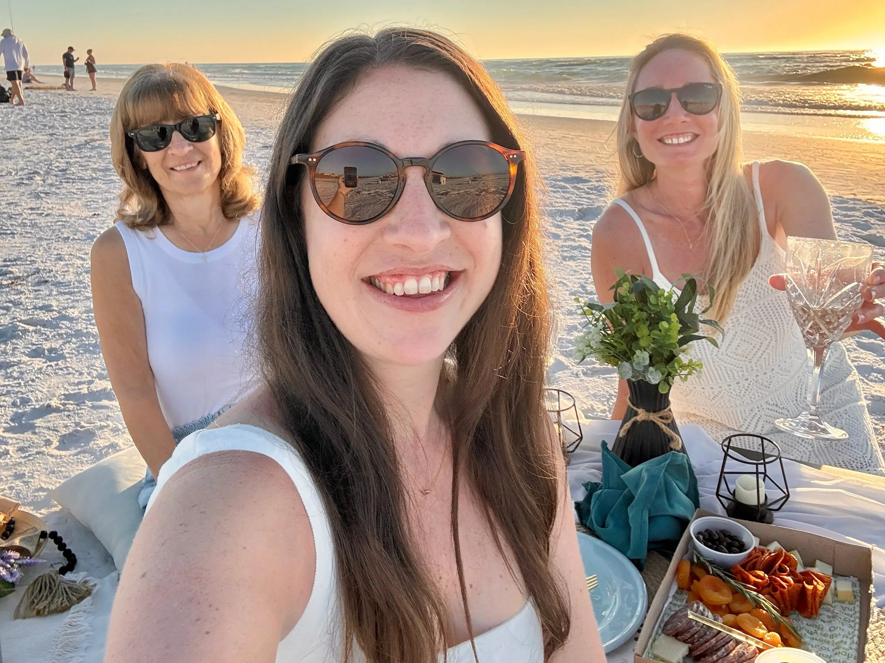 Three women with sunglasses smiling in selfie on beach